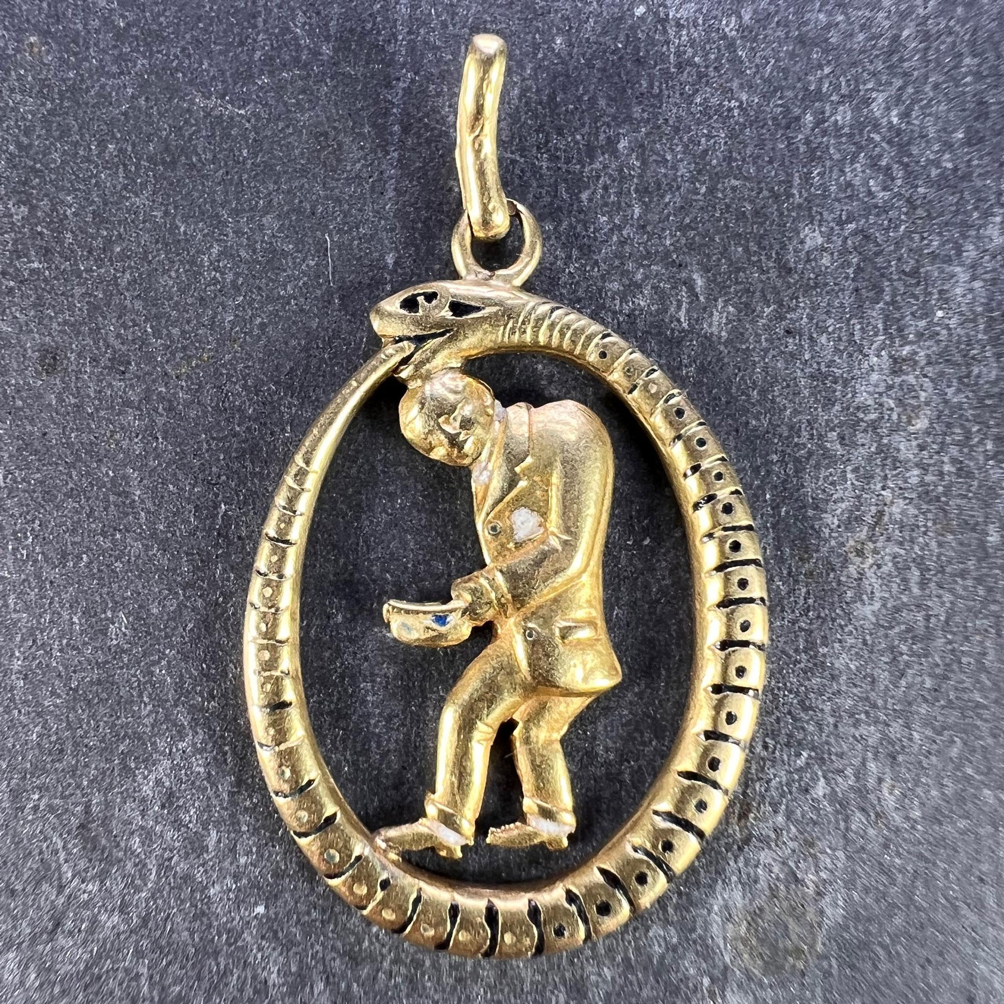 An 18 karat (18K) yellow gold and enamel charm pendant designed as an Ouroboros snake or serpent eating its own tail encircling a man in a suit holding a hat. Stamped K18 for 18 karat gold to the reverse with French import marks and an unknown
