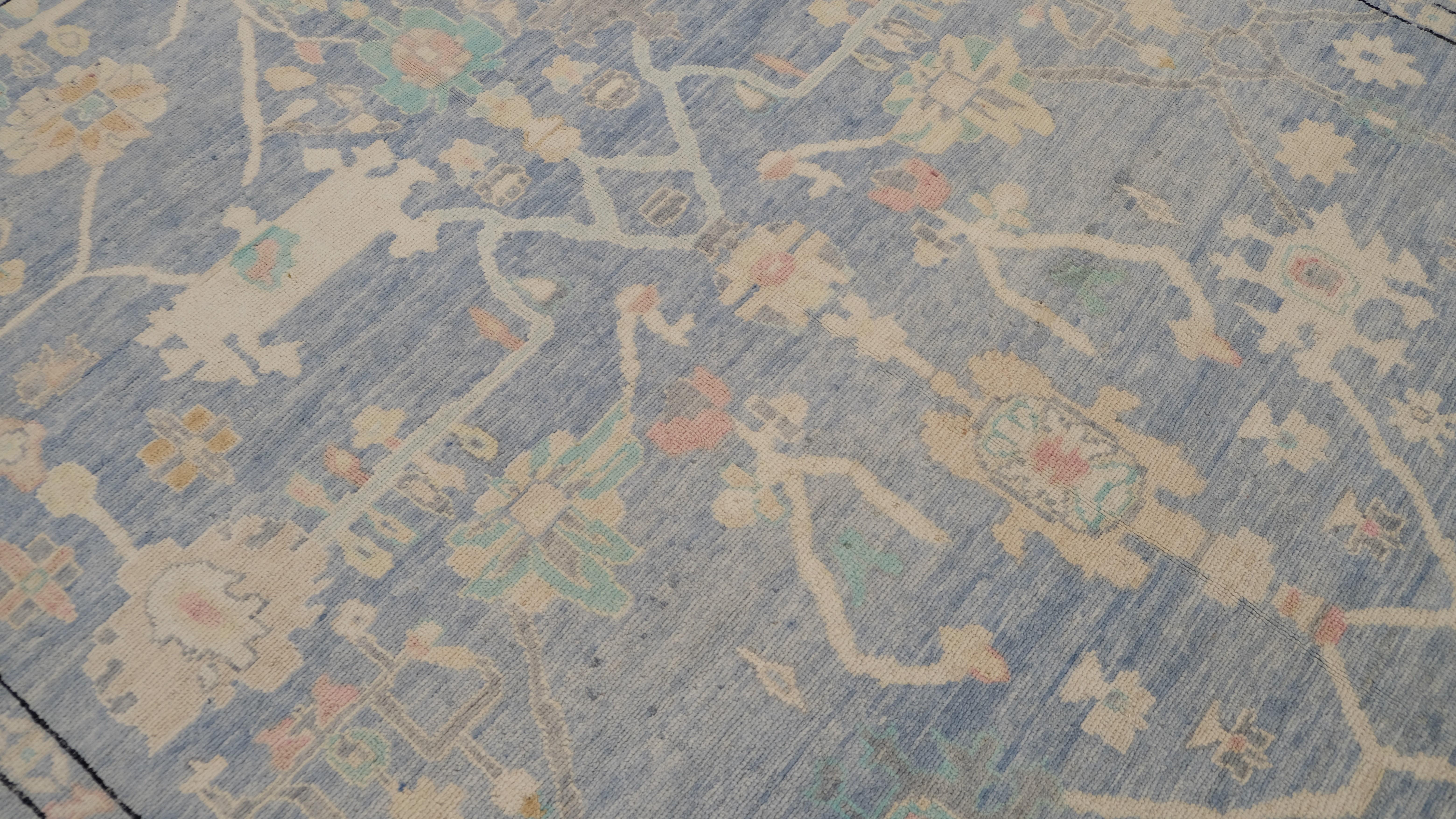 Esta alfombra de lana anudada a mano es un asombroso ejemplo del diseño tradicional Oushak, reimaginado en una paleta de colores suaves y apagados de tonos azules, marfil y rosa. Los intrincados motivos florales y geométricos, delicadamente