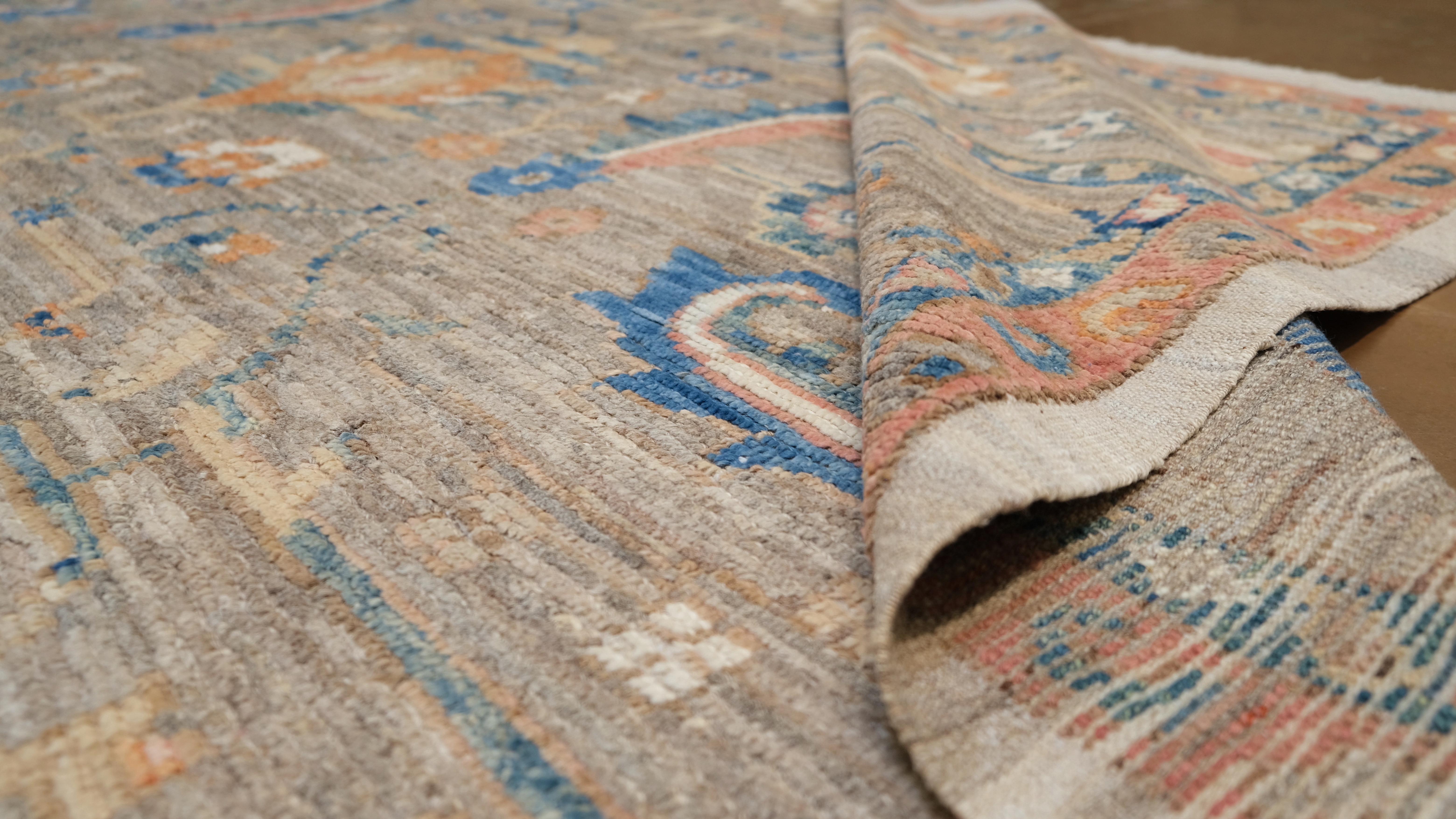 Ce tapis en laine nouée à la main rehausse votre intérieur. D'inspiration oushak, ce tapis présente des motifs floraux et de vigne complexes, ornés de nuances de bleu, de corail et d'un fond taupe. La bordure détaillée encadre le médaillon central