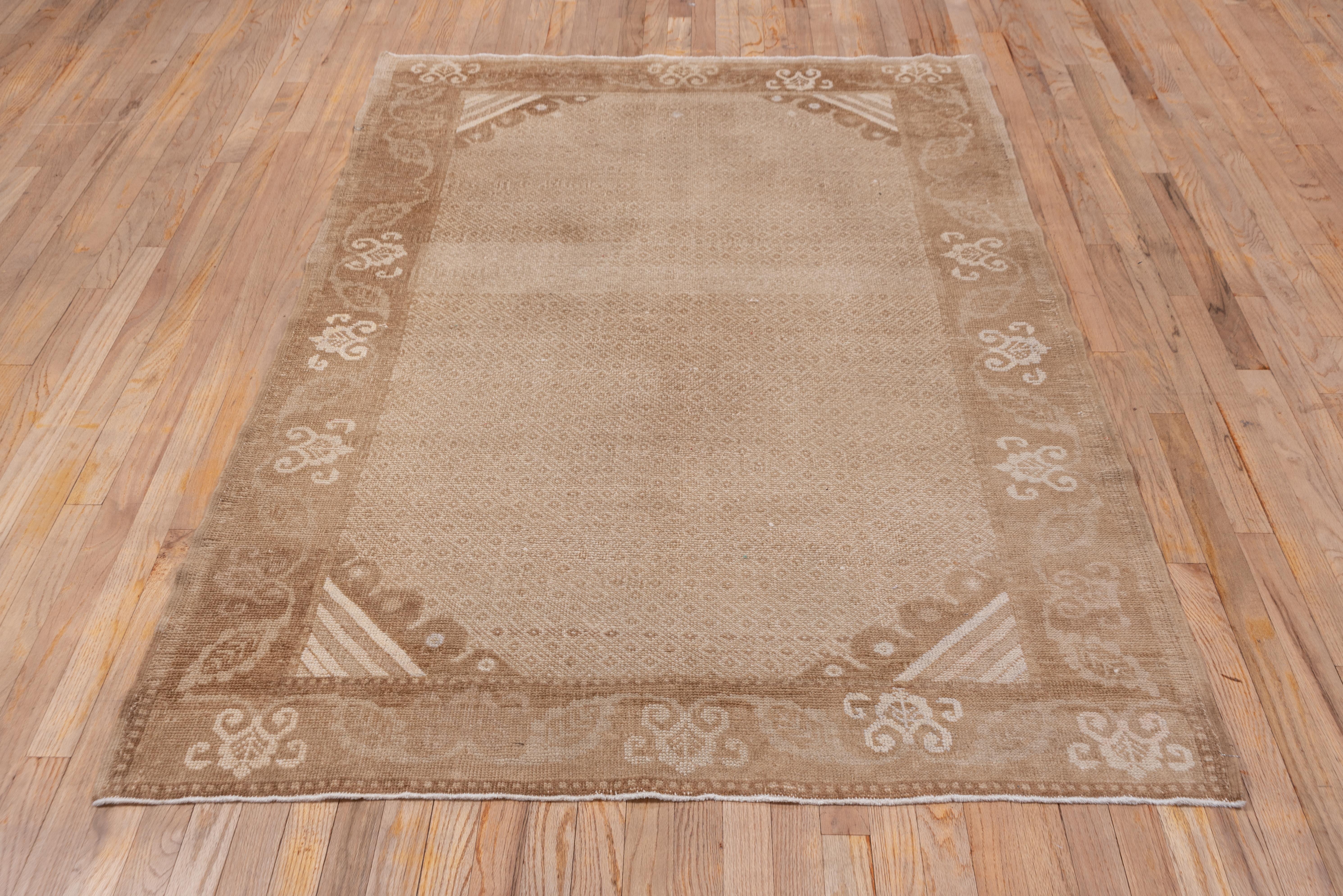 The field shows a small doubled lozenge pattern enclosing little diamonds in beige and light brown, with boldly striped corners, and set within a wide buff border with voluted reversing simple palmettes with ivory details.