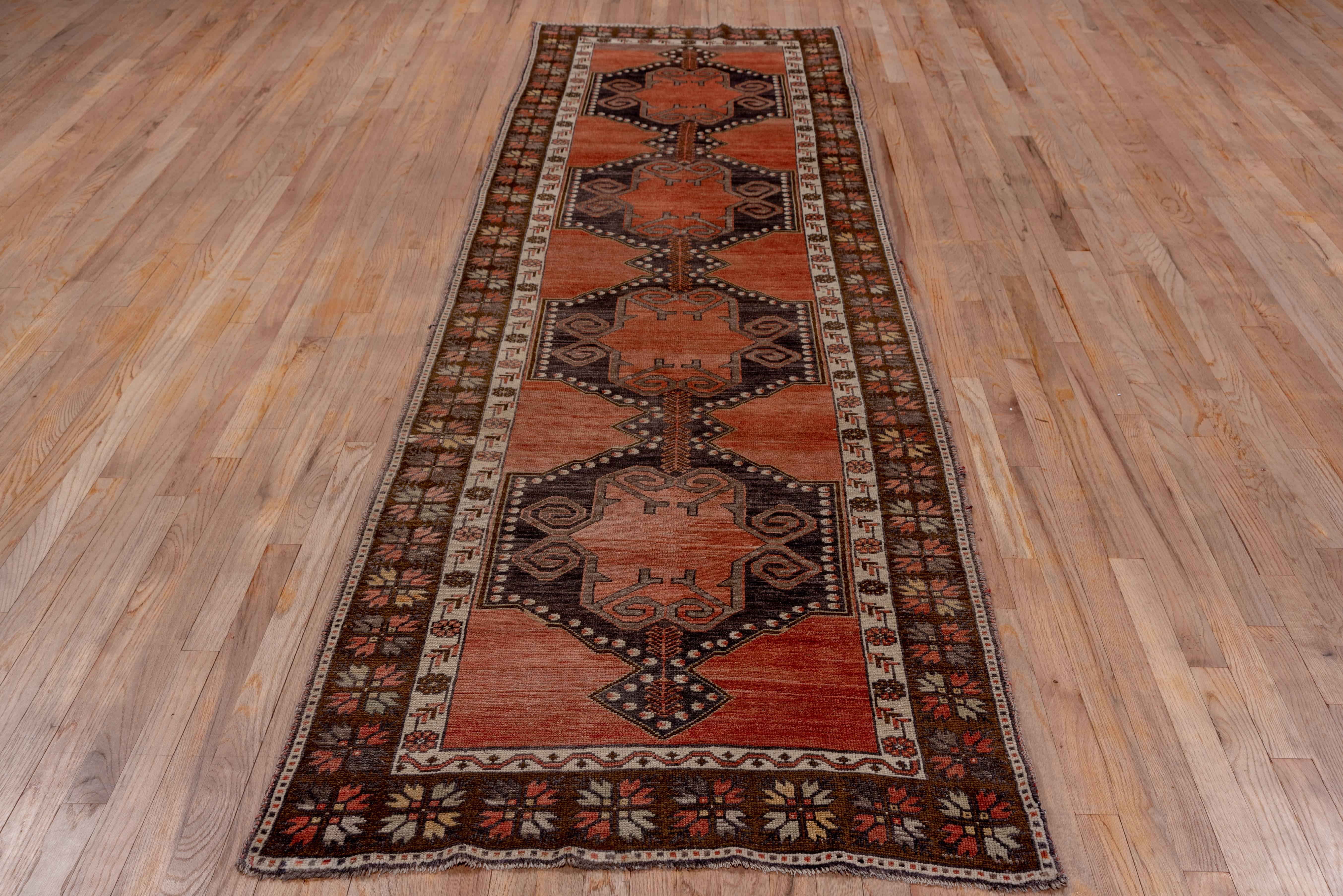 This central Anatolian all wool runner has an abrashed brown field decorated with a pole medallion of dark brown conjoint hexagons enclosing gull like motives. The dark brown border of four bud rosettes is a characteristic of central Turkish rugs.