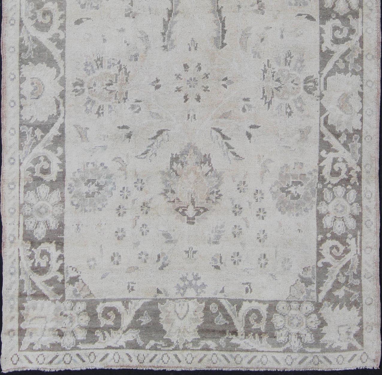 Handwoven in mid-20th century Turkey, this vintage Oushak carpet is built on traditional designs and features an all-over botanical pattern in its central field. Rendered in gray and cream tones, this carpet beautifully communicates the finer