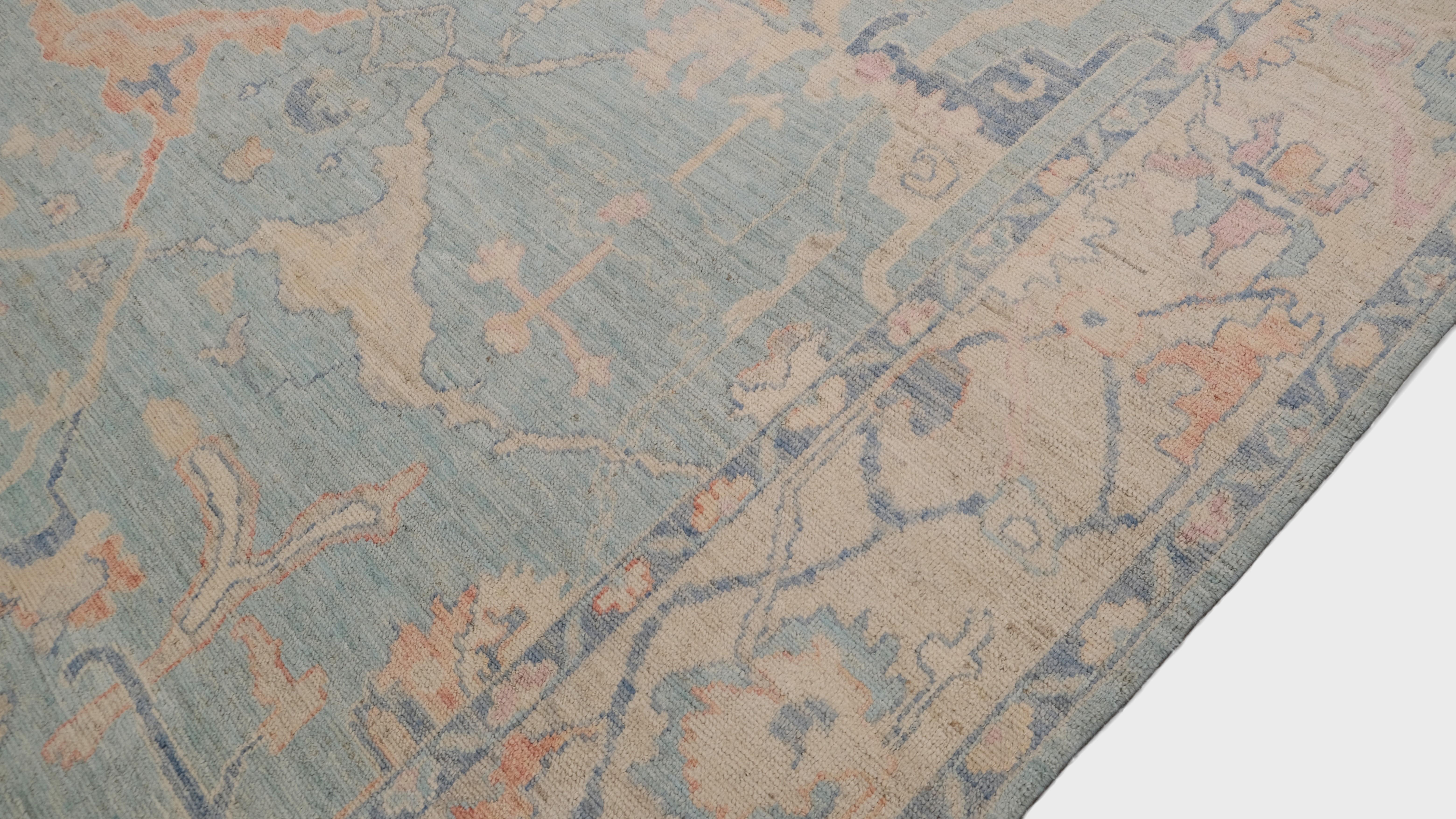Esta alfombra de lana anudada a mano presenta un precioso diseño Oushak, que combina la elegancia tradicional con una estética vintage contemporánea. Los intrincados motivos florales y enredaderas, tejidos en una delicada y suave paleta de azul