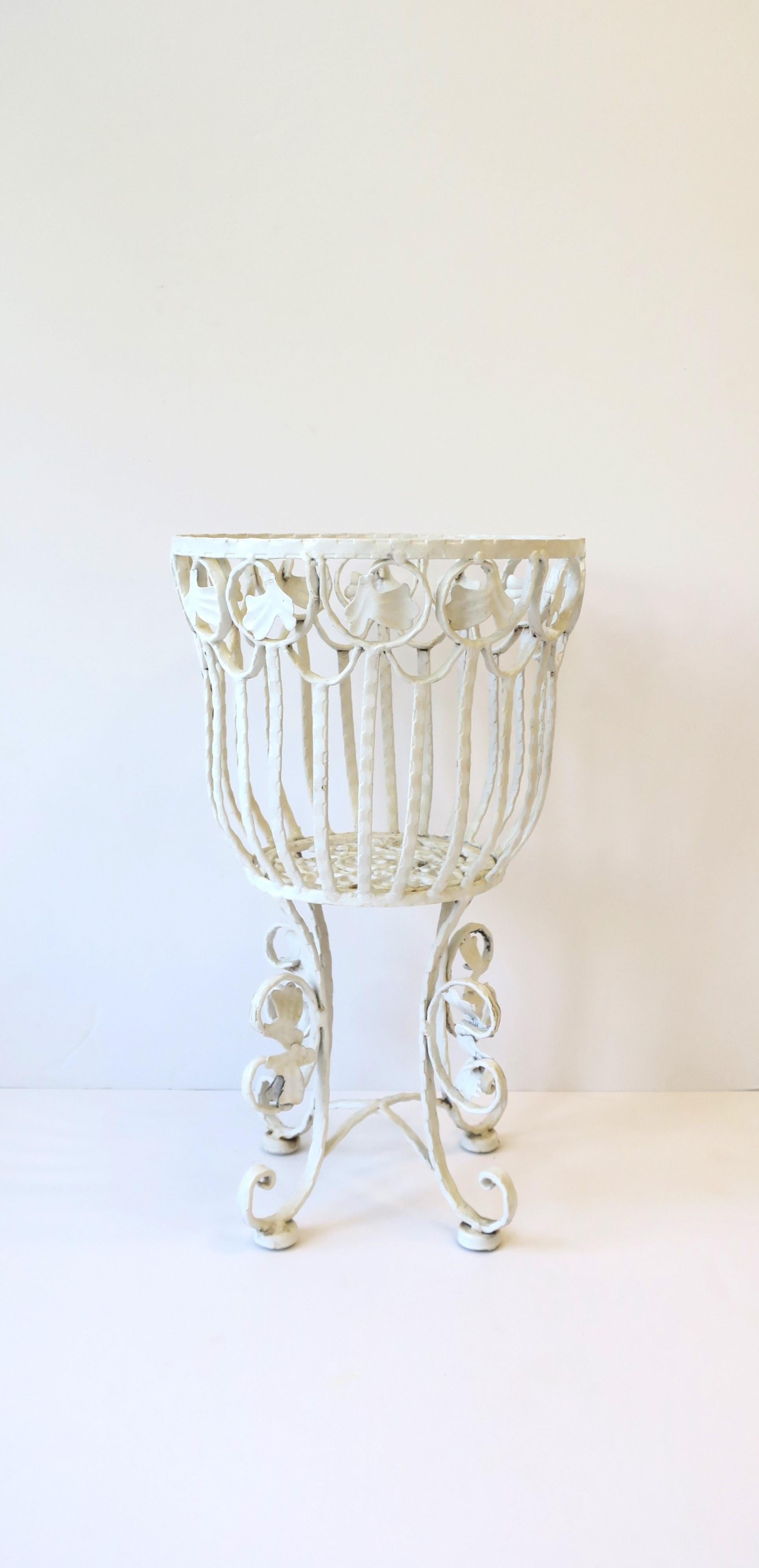 A substantial vintage outdoor garden or patio white cachepot flower or plant pot holder stand, circa mid-20th century, USA. Piece is painted wrought iron with 'basket' area for pot, leaf design near top of basket, and scrolled feet with leaves at