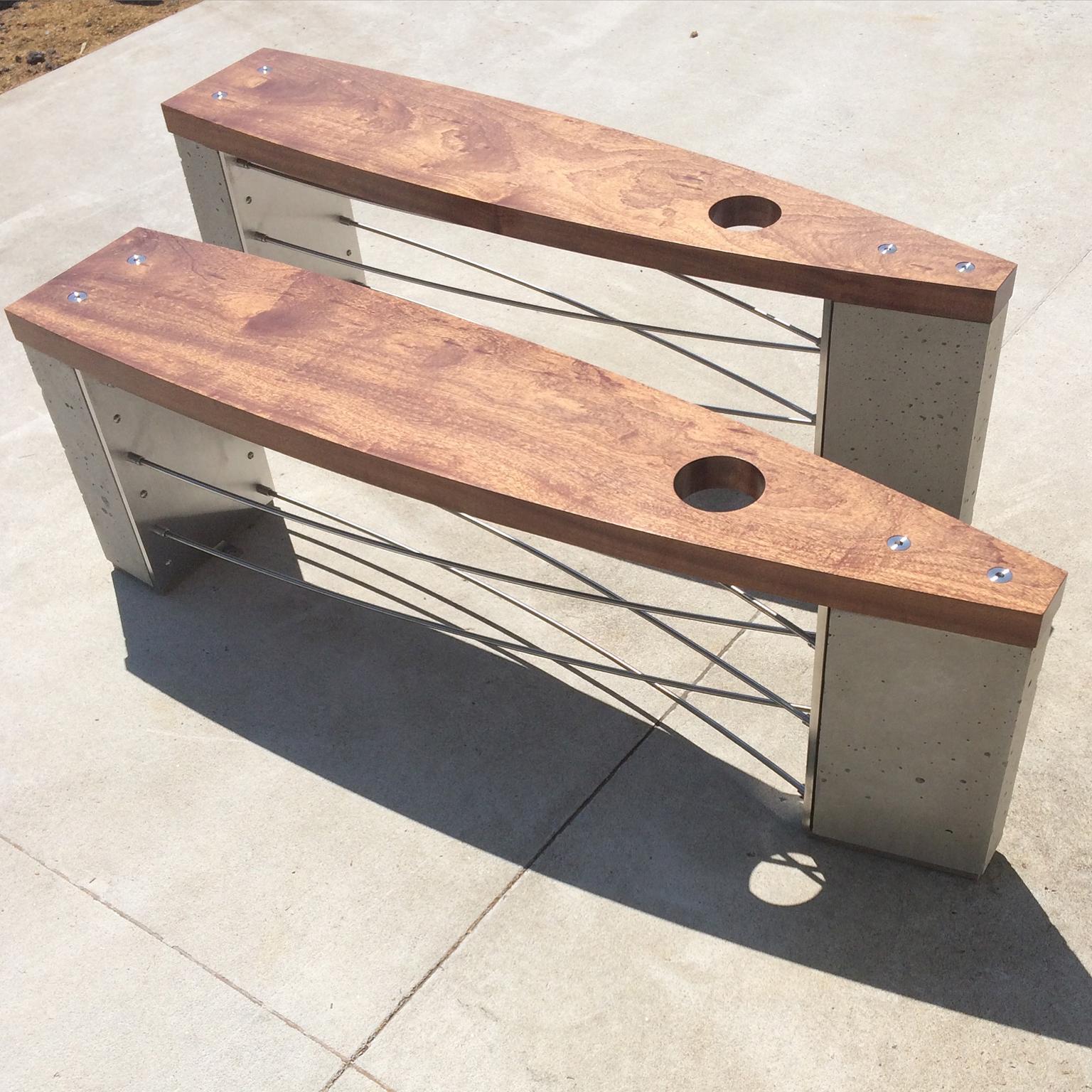 This is an outdoor version of the Classic Jupiter bench by Peter Harrison. It is constructed of concrete, stainless steel, and mahogany and specifically intended for exterior use. Its design has nautical references. The hole through the top centers
