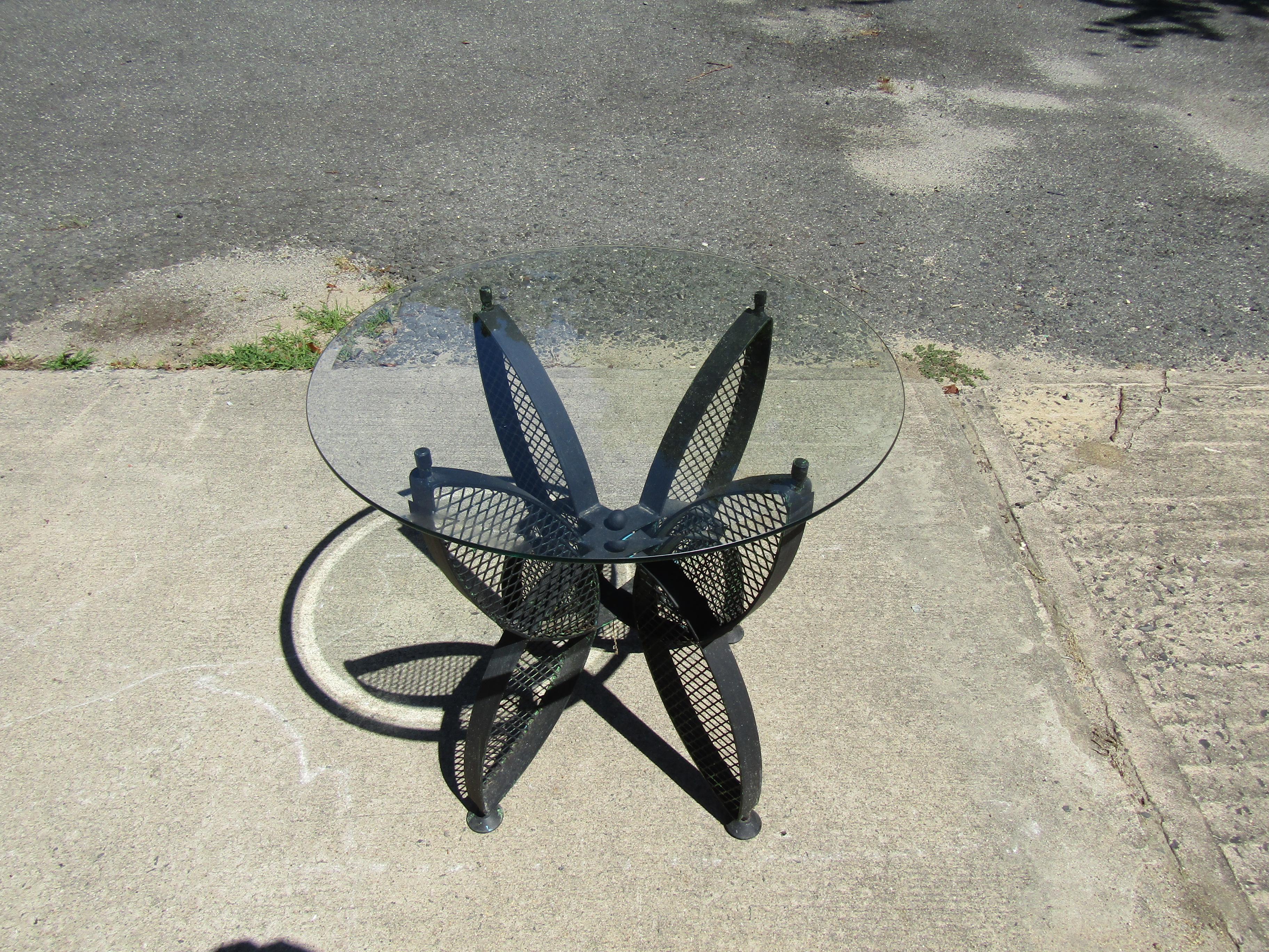 Dieser Tisch für den Außenbereich kombiniert ein einzigartiges Metallgestell mit einer runden Glasplatte und eignet sich perfekt für eine Terrasse oder einen Garten. 
Bitte bestätigen Sie den Standort des Artikels mit dem Verkäufer (NY/NJ).