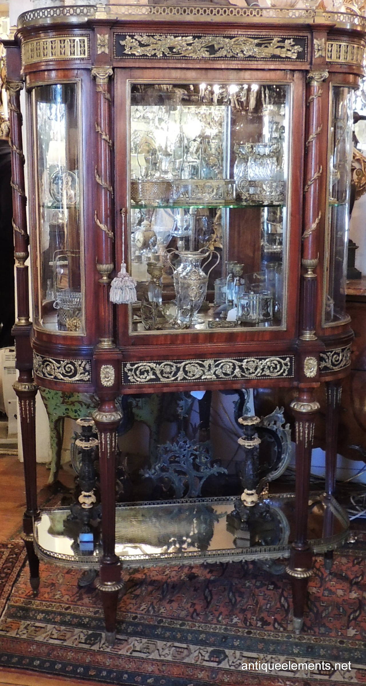 This beautiful Classic is an early 1900s French rosewood vitrine with beautiful bronze ormolu-mounted details. There are two glass shelves in the top portion with a wonderful mirrored back. The side glasses are original and curved, set off with the