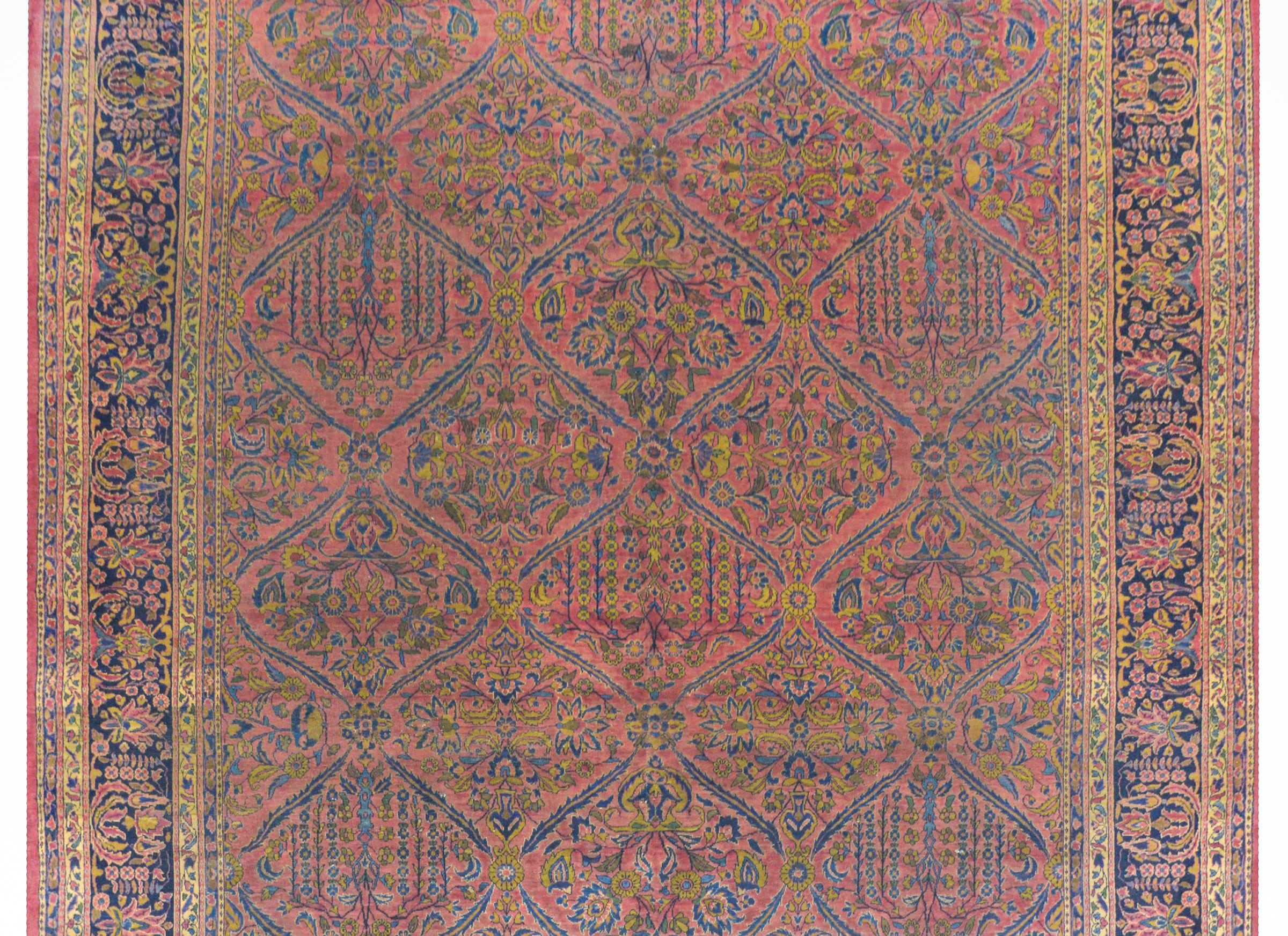 An outstanding early 20th century Persian Sarouk rug with a fantastic all-over trellis pattern containing weeping willows trees and potted blossoming flowers and vines all woven in light and dark indigo, and gold on a cranberry colored background.