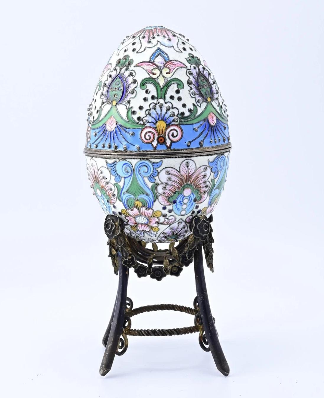 Este exquisito huevo decorativo de esmalte ruso es una cautivadora obra de arte. El huevo presenta un intrincado diseño con colores vibrantes, como el azul, el rosa y el verde, sobre un fondo blanco. Los motivos ornamentales están meticulosamente