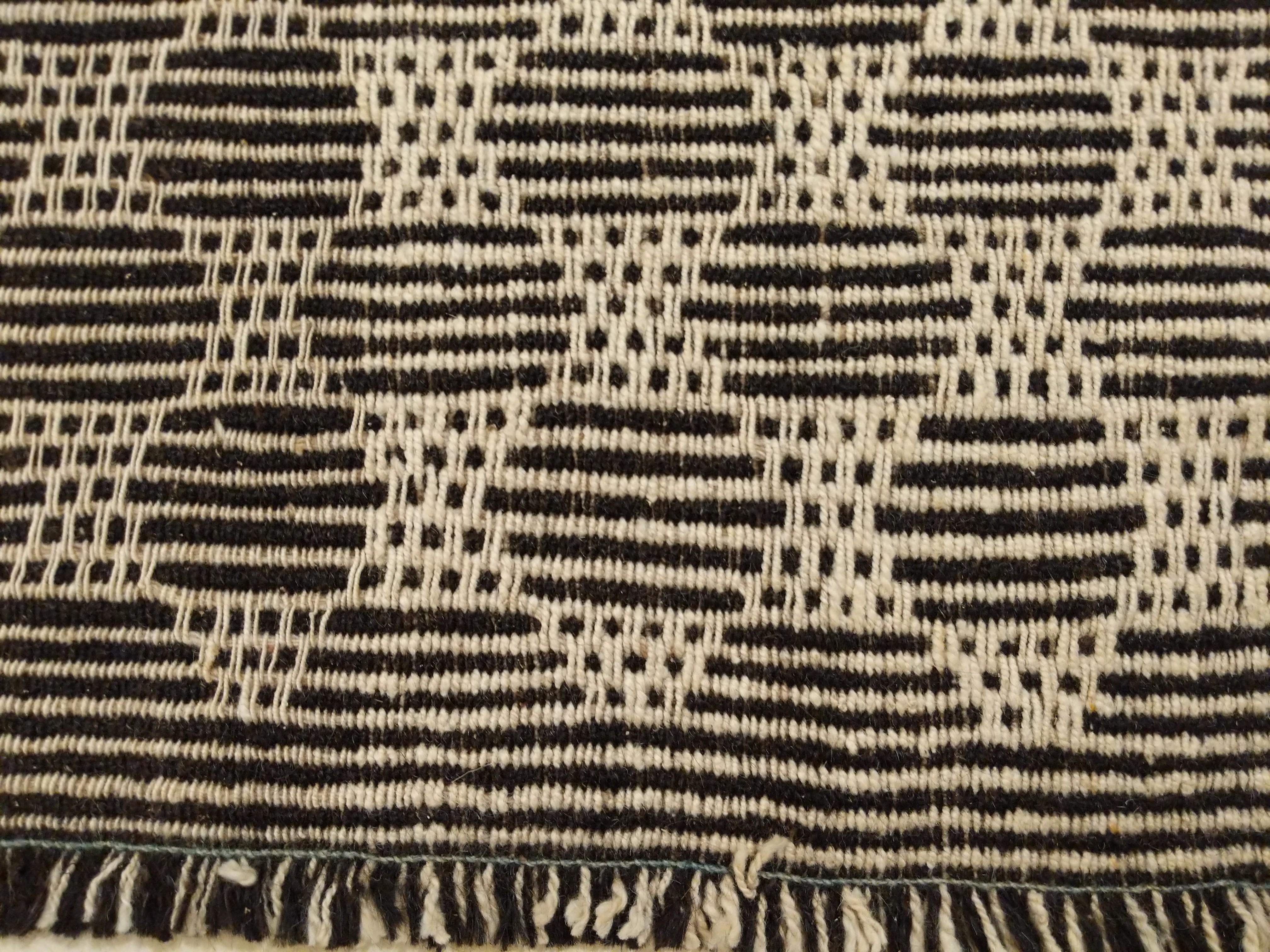 A stunning wool kilim handwoven in the style of the antique tribal flat-weaves, distinguished by a background woven in three panels and composed of thin, alternating stripes in ivory and dark brown/black onto which is laid a filigree-type of