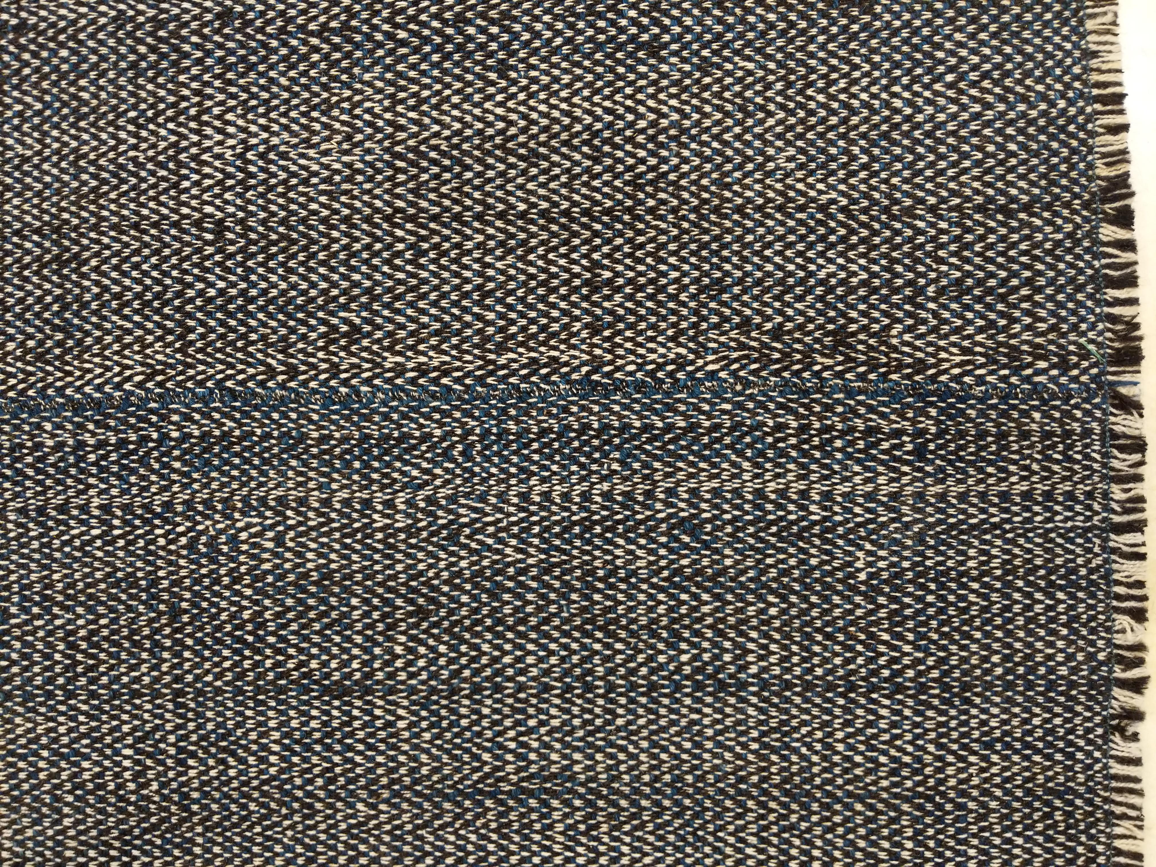 A stunning wool kilim handwoven in the style of the antique tribal flat-weaves, distinguished by a careful miscellany of hand-spun wool threads in dark blue, black and ivory, creating a highly elegant tweed-like pattern. The piece is woven on three