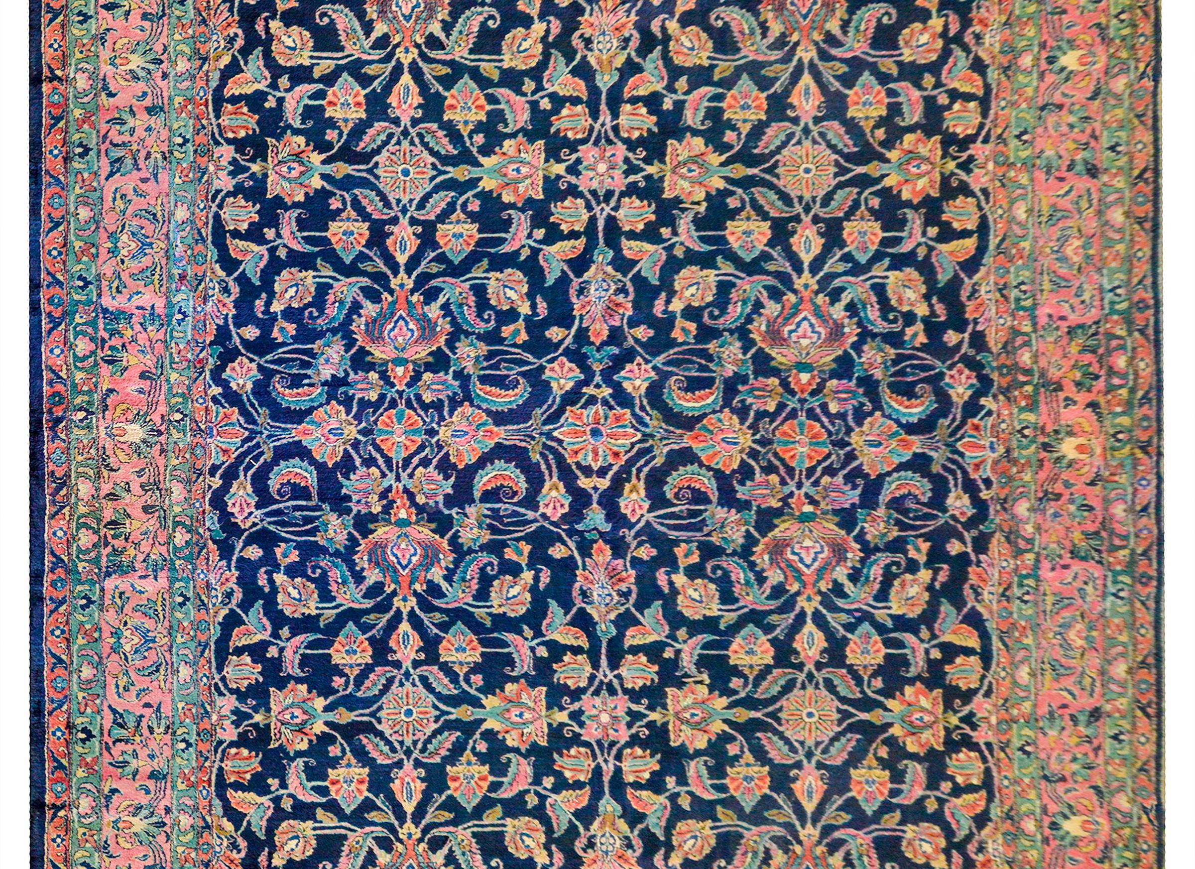 An absolutely incredible early 20th century antique Persian Sarouk rug with an all-over mirrored floral and scrolling vine lattice pattern woven in orange, pink gold, and light and dark indigo, on a dark indigo background. The border is wonderful