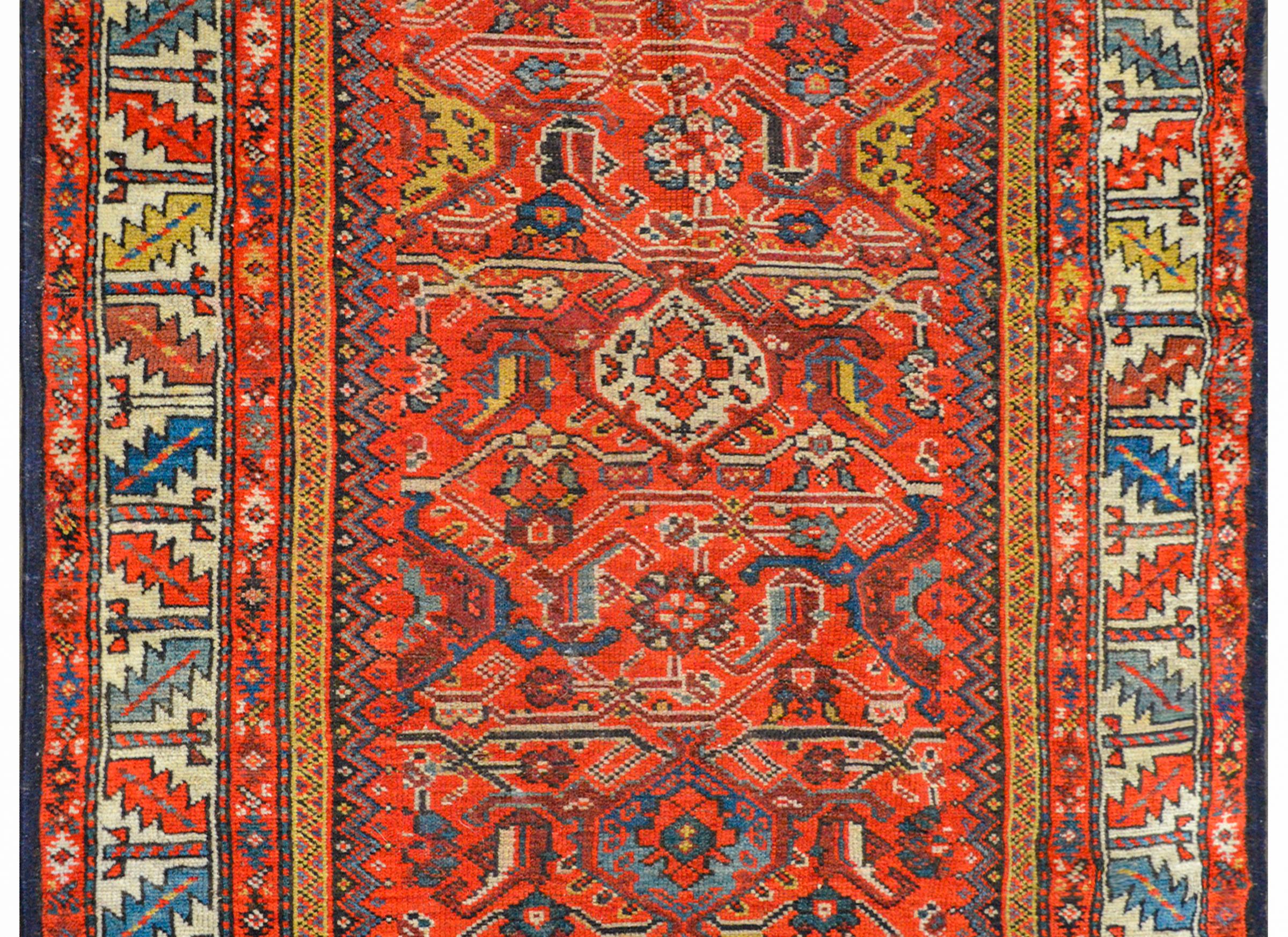 An outstanding early 20th century Azerbaijani Azari Herati runner with a large scale pattern of stylized flowers, vines, and leaves woven in light and dark indigo, crimson, white, and gold on a rich crimson background. The border is composed of