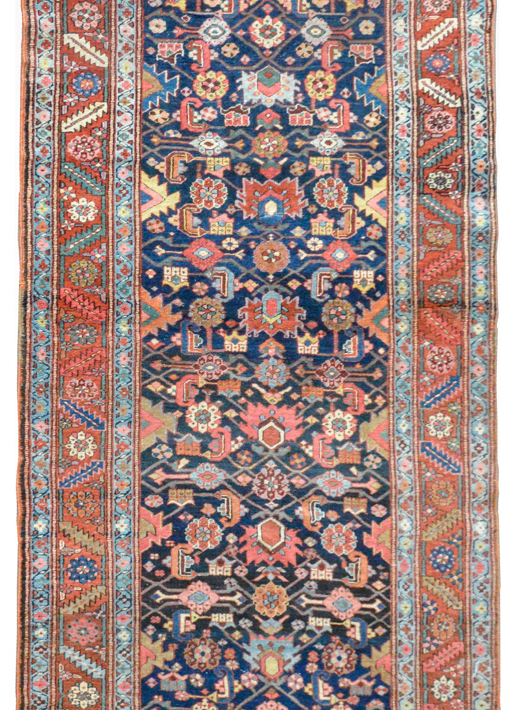 An outstanding early 20th century Persian Heriz runner with a bold stylized floral lattice pattern woven in light indigo, crimson, coral, gold, and crimson, all against a dark indigo background. The border is exceptional with a stylized leaf and