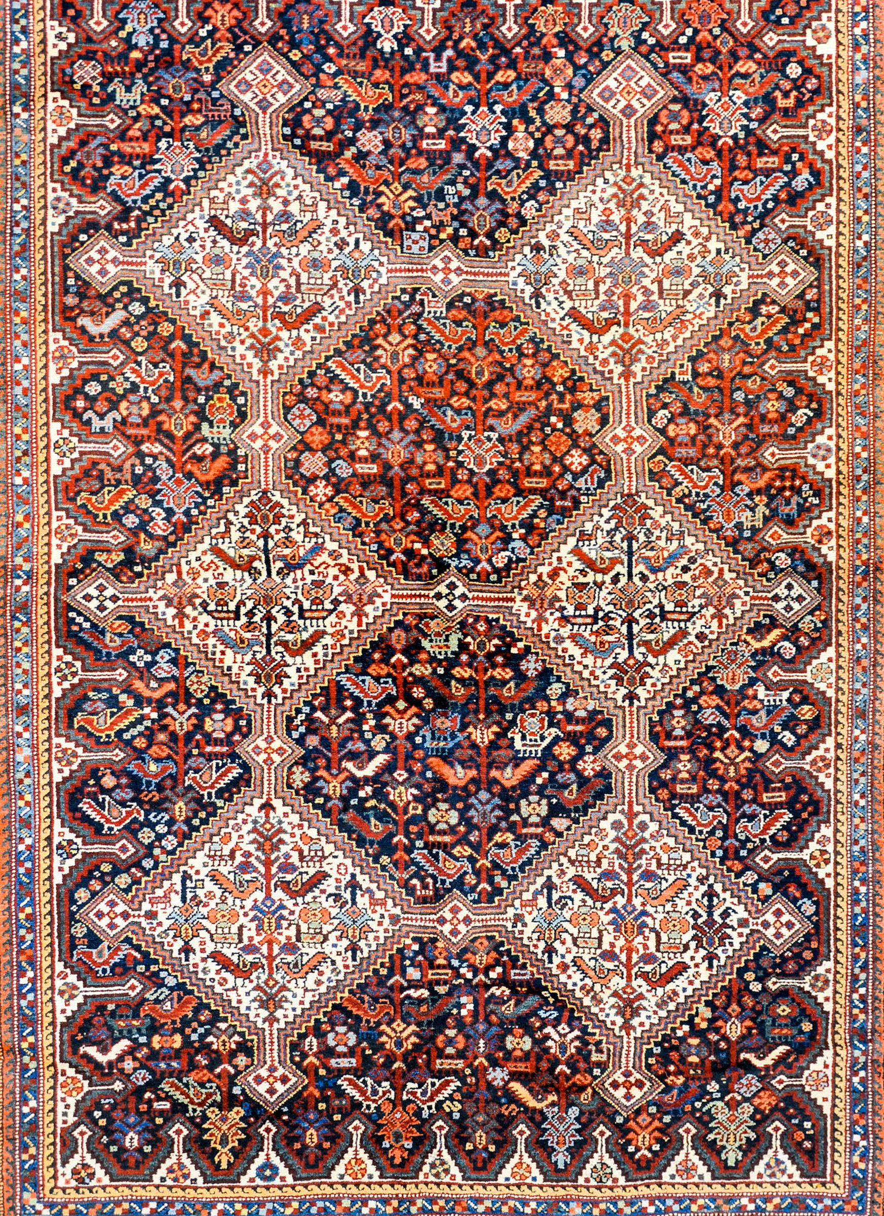 An outstanding early 20th century Persian Kamseh rug with six large white diamond medallions filled with densely woven stylized flowers and chickens on a black field of similarly styled flowers and chickens woven in myriad colors. The border is