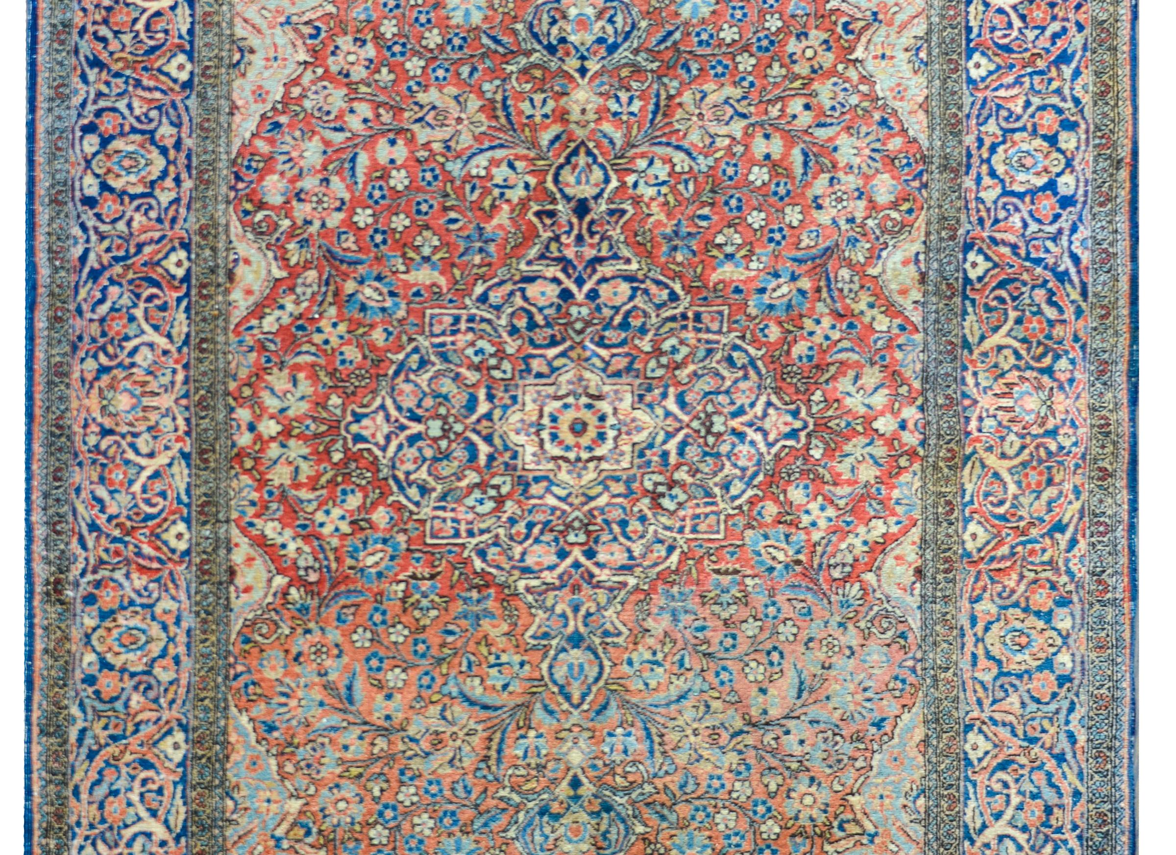An outstanding early 20th century Persian Kashan rug with the most elaborate central medallion and floral field woven in beautiful indigos, pinks, golds, and creams set against a fantastic abrash red background. The border is equally beautiful with