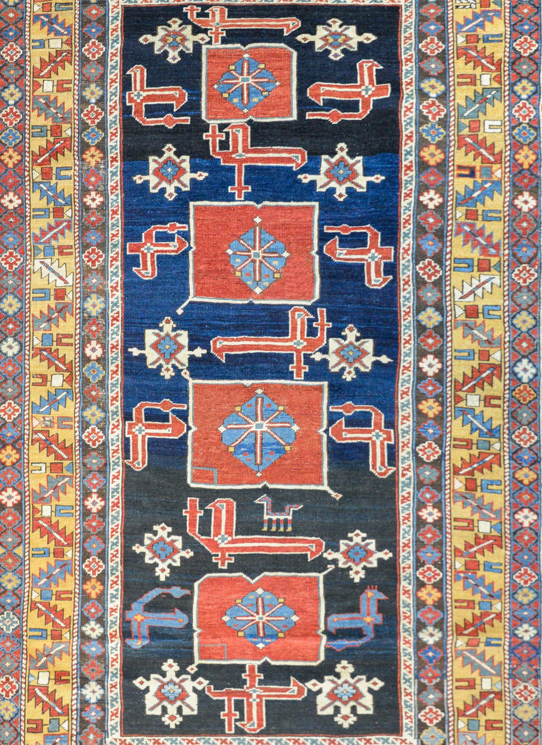 An outstanding early 20th century Azerbaijani Kazak rug with a bold pattern containing four large crimson medallions amidst a field of stylized flowers and scrolling vines on a beautiful rich dark Abrash indigo background. The border is exceptional