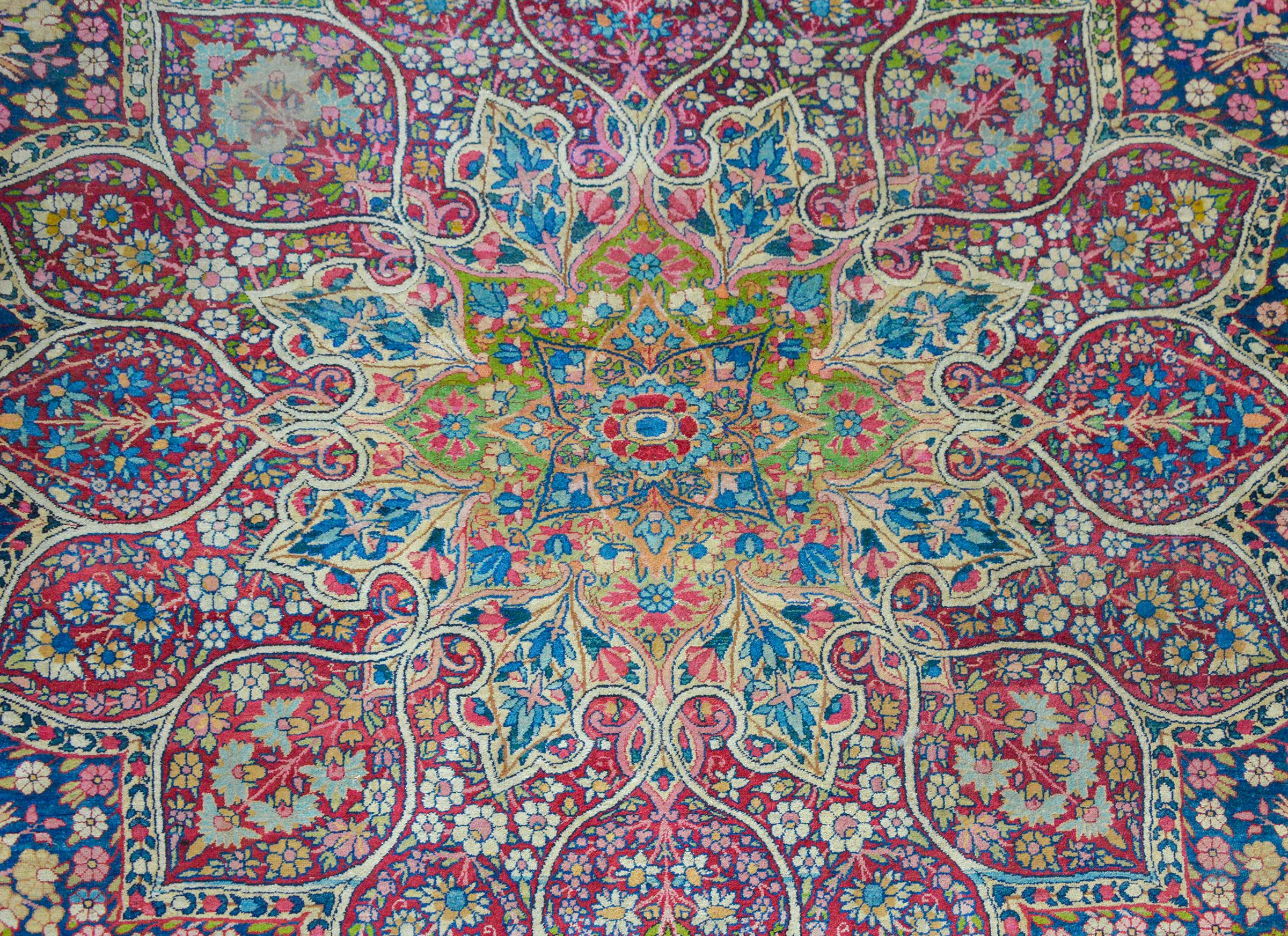 An outstanding early 20th century Persian Lavar Kirman rug with a mesmerizing pattern reminiscent of a stained-glass window woven with bold pinks, blues, reds, greens, and golds, amidst a field of scrolling vines and flowers and all set against a