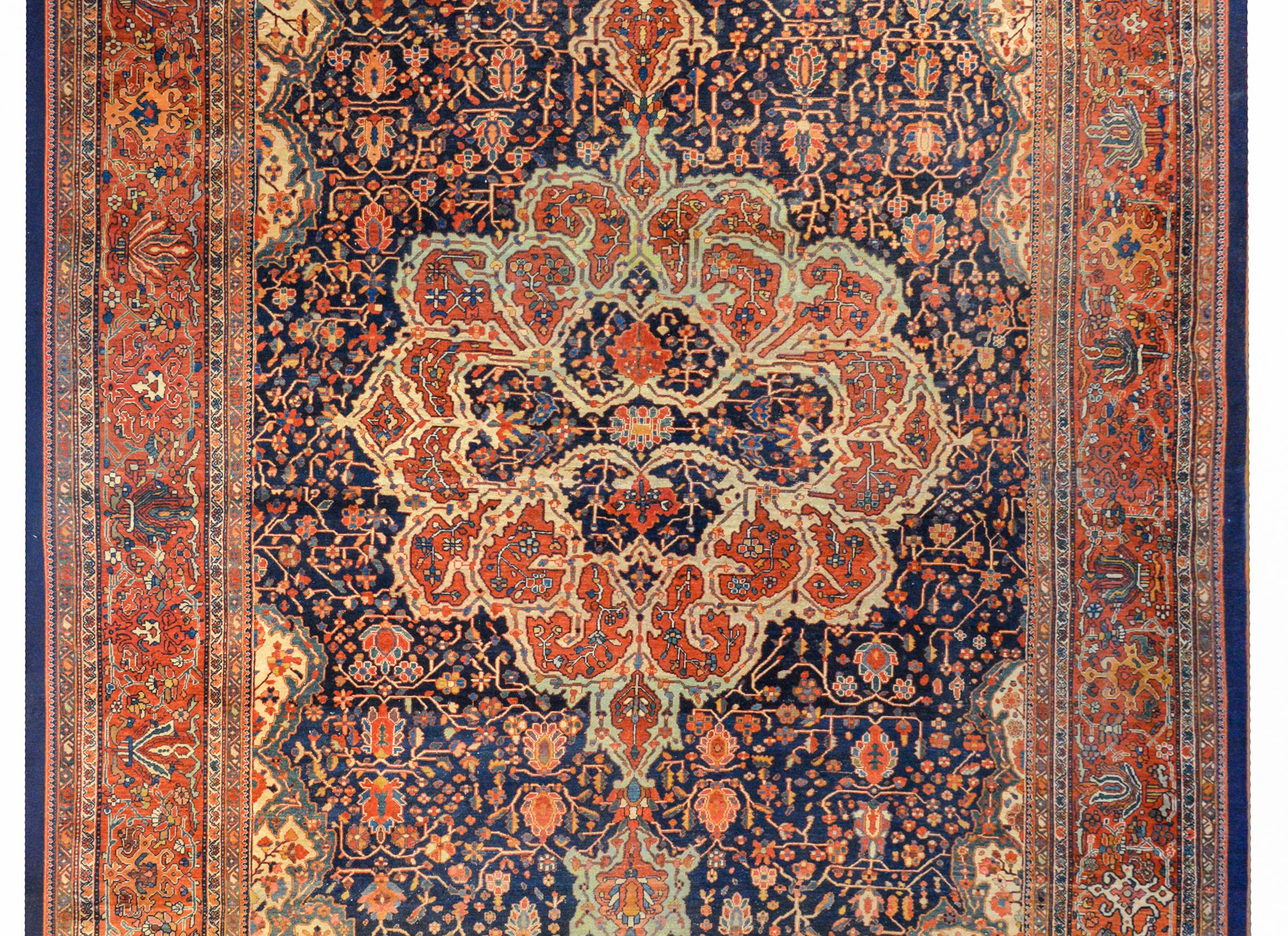 An extraordinary early 20th century Persian Sarouk Farahan rug with a wonderfully woven abstract medallion woven in myriad flowers and vines with a crimson background, all on a field of more flowers and vines on a dark indigo background surrounded