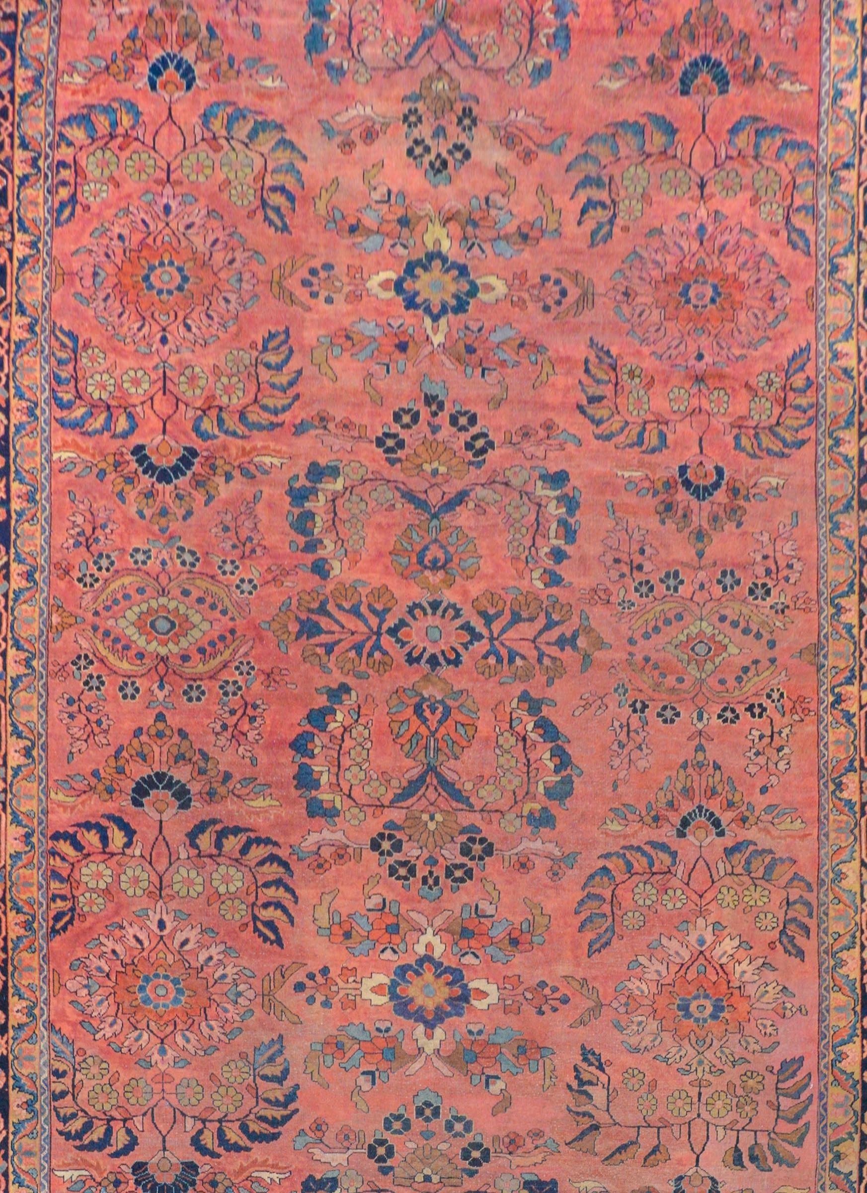An outstanding early 20th century Persian Sarouk Mahal rug woven with a fantastic large-scale mirrored pattern of flowers and leaves woven in light and dark indigo, cream, crimson, and gold on a pale cranberry background surrounded by a wonderful