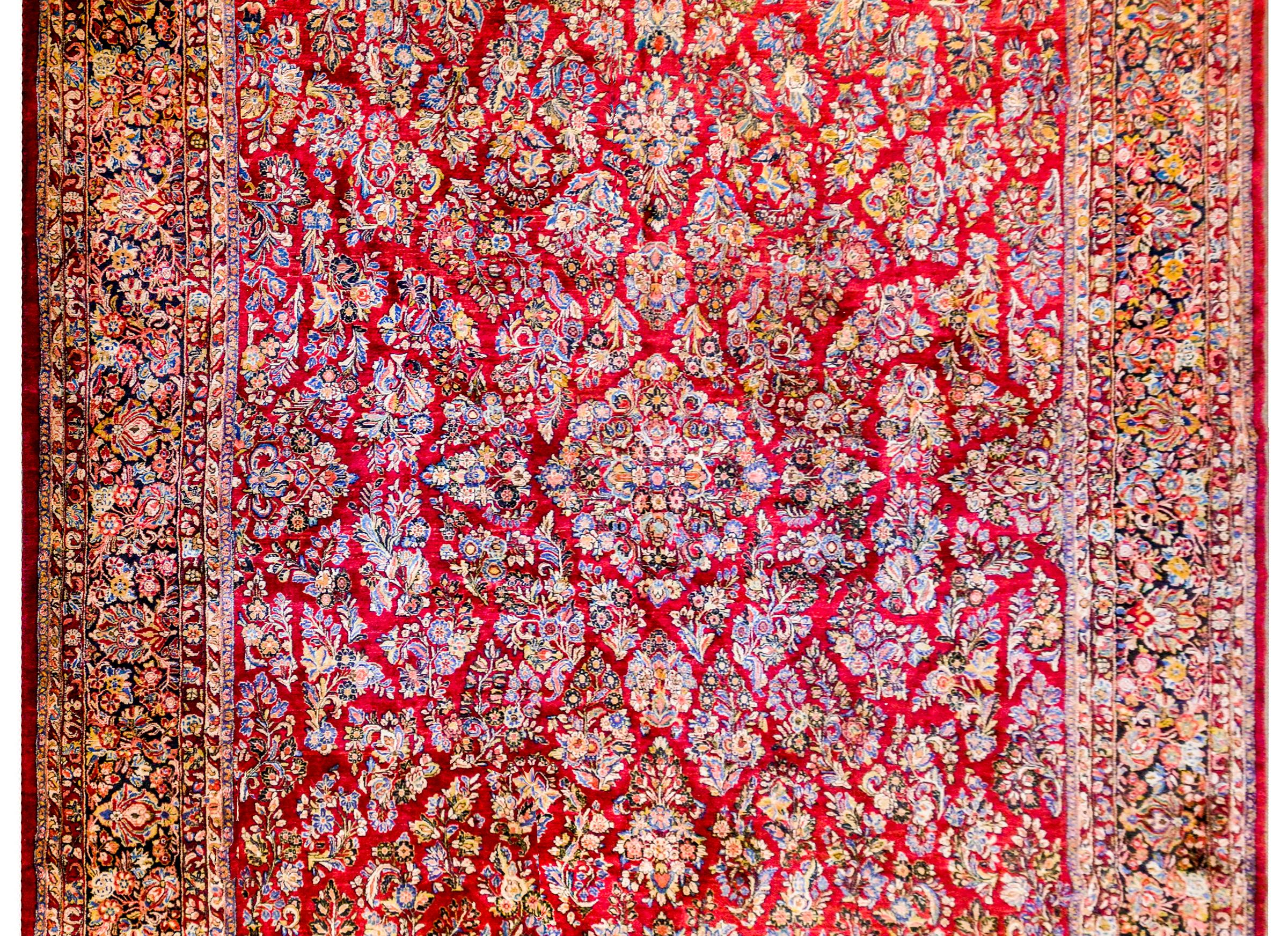 An outstanding early 20th century Persian Sarouk rug with an amazing mirrored myriad floral and leave pattern woven in light and dark indigo, gold, pink, and orange colored wool on a deep crimson backgound. The border is complex with a wide, densely