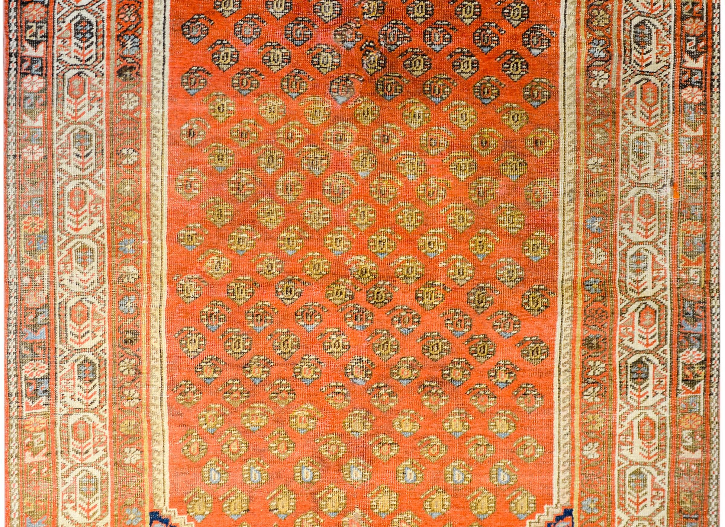An early 20th century Persian Seraband rug with an amazing all-over paisley pattern woven in an incredible brilliant orange, gold, light indigo, and cream colored wool on a rusty orange colored wool background. The border is complex with multiple