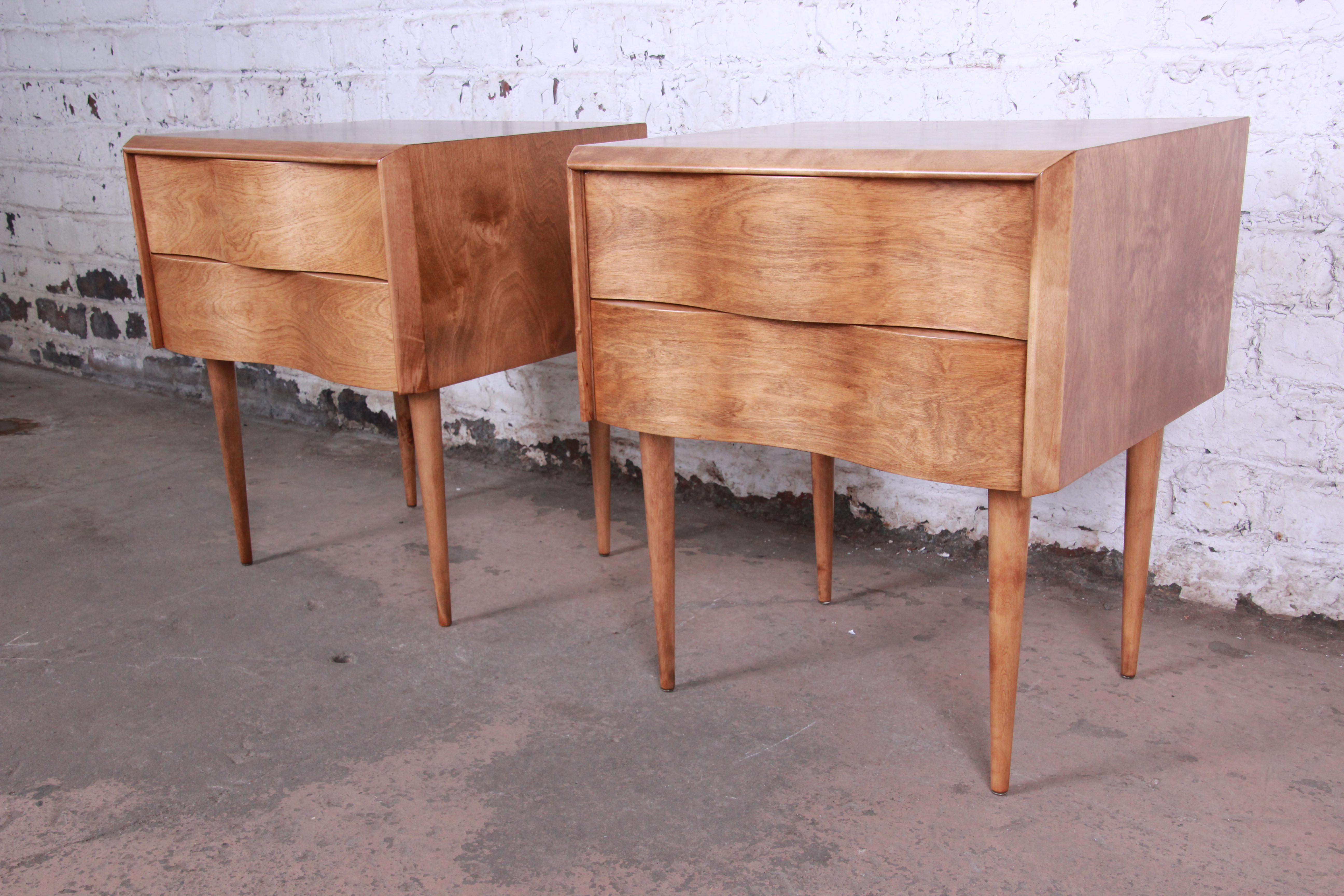 Offering a rare and exceptional pair of Mid-Century Modern nightstands designed by Edmond Spence. The nightstands feature a unique wave front design and stunning birchwood grain. They offer good storage, each with two deep dovetailed drawers. The