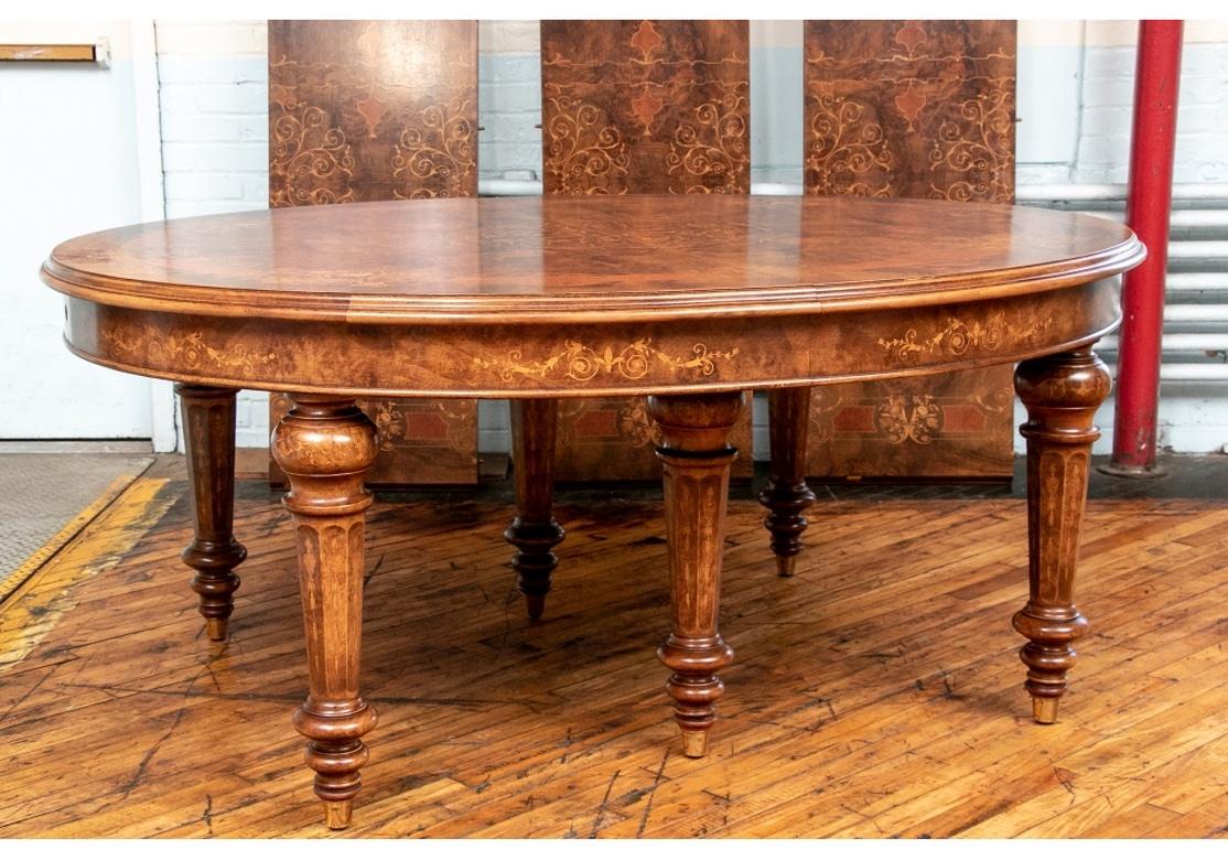 A large oval burled table with overall elaborate marquetry decoration. With a two-tone banded top with floral scrolled marquetry elements, some with musical motifs. The center with a large medallion with pale foliate scrolls and pendant shield