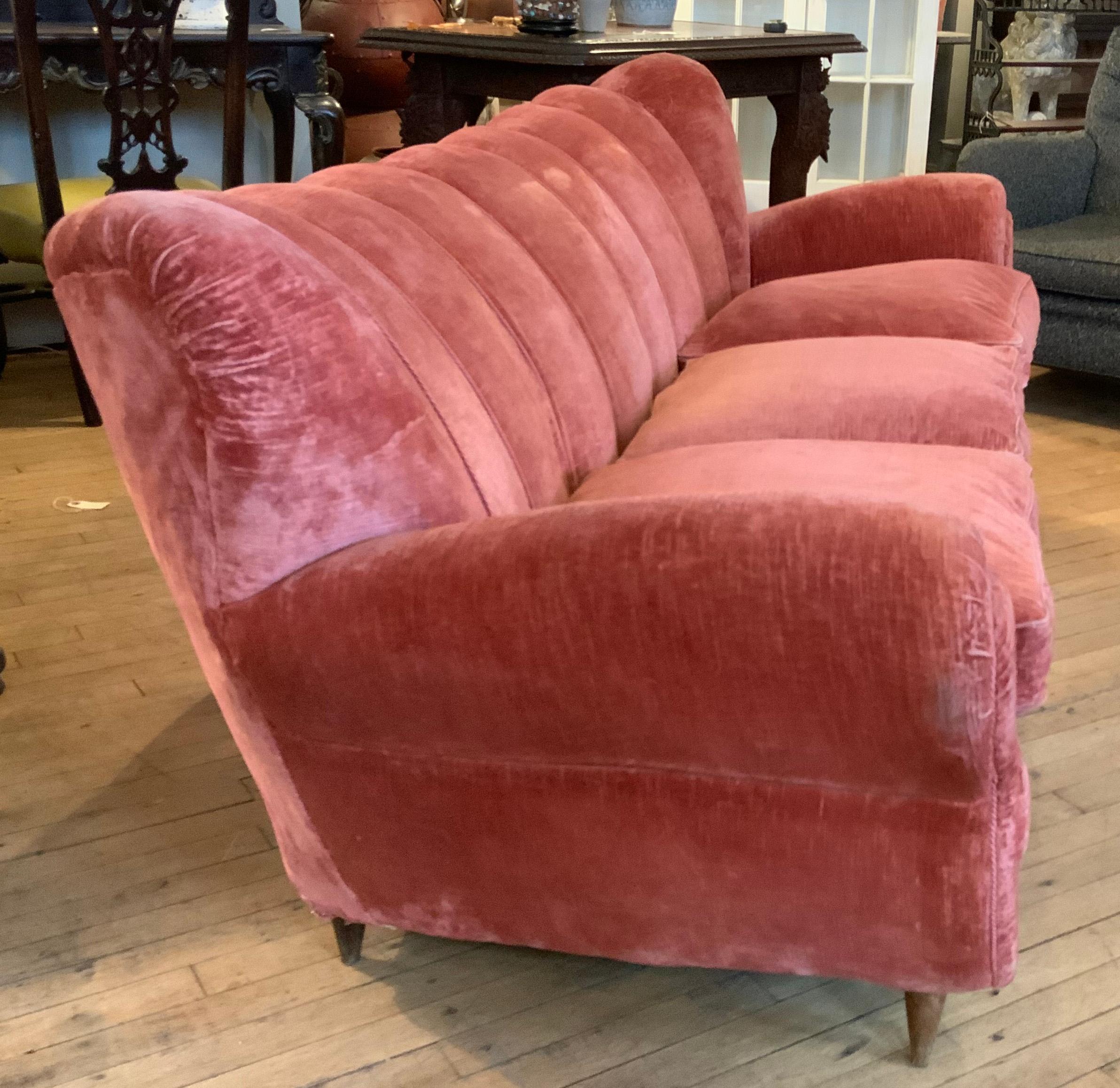 A truly incredible 1940's Italian upholstered sofa, with large scrolled arms, and channel upholstered back. wonderful design and scale, in it's original pink/salmon colored velvet fabric, which shows age expected wear. the sofa is raised on tapered