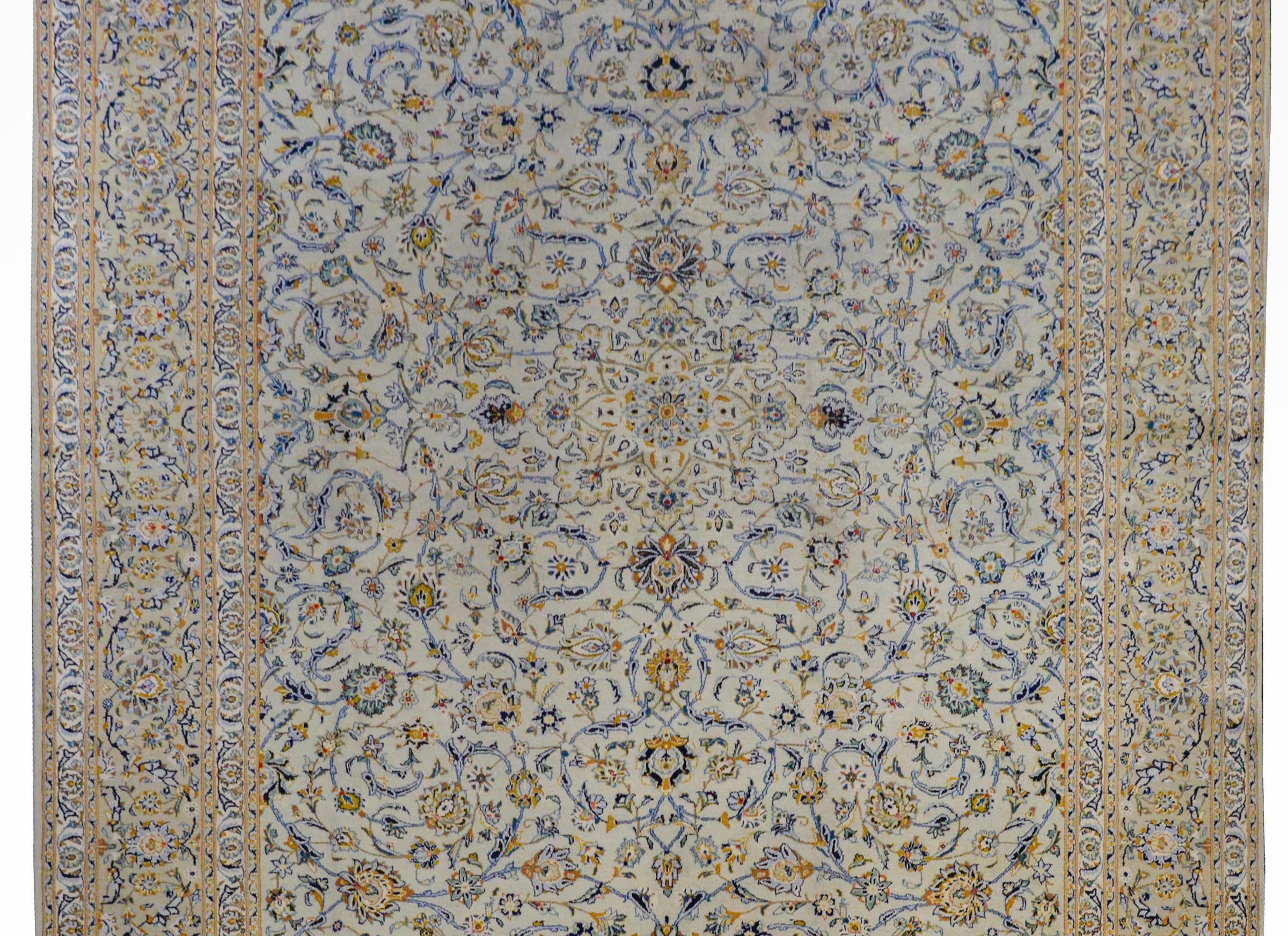 An outstanding mid-20th century Persian Kashan rug with an all-over floral and scrolling vine trellis pattern woven in light and dark indigo, green, gold, orange, and red vegetable dyed wool on a cream colored ground. The border is exceptionally
