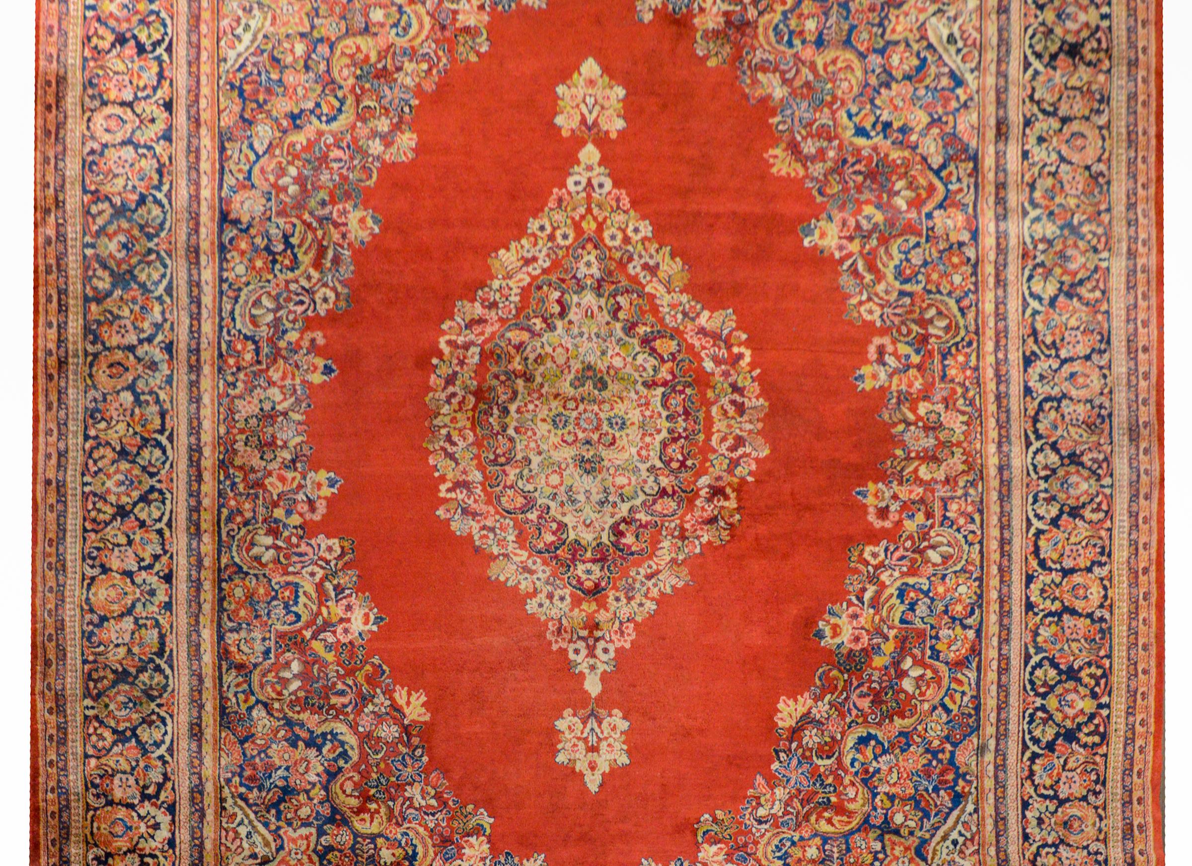 An outstanding monumental early 20th century Persian Sarouk rug with a large floral medallion woven in myriad colors including green, indigo, violet, pink, and cream on a brilliant coral colored background all surrounded by a lush floral border