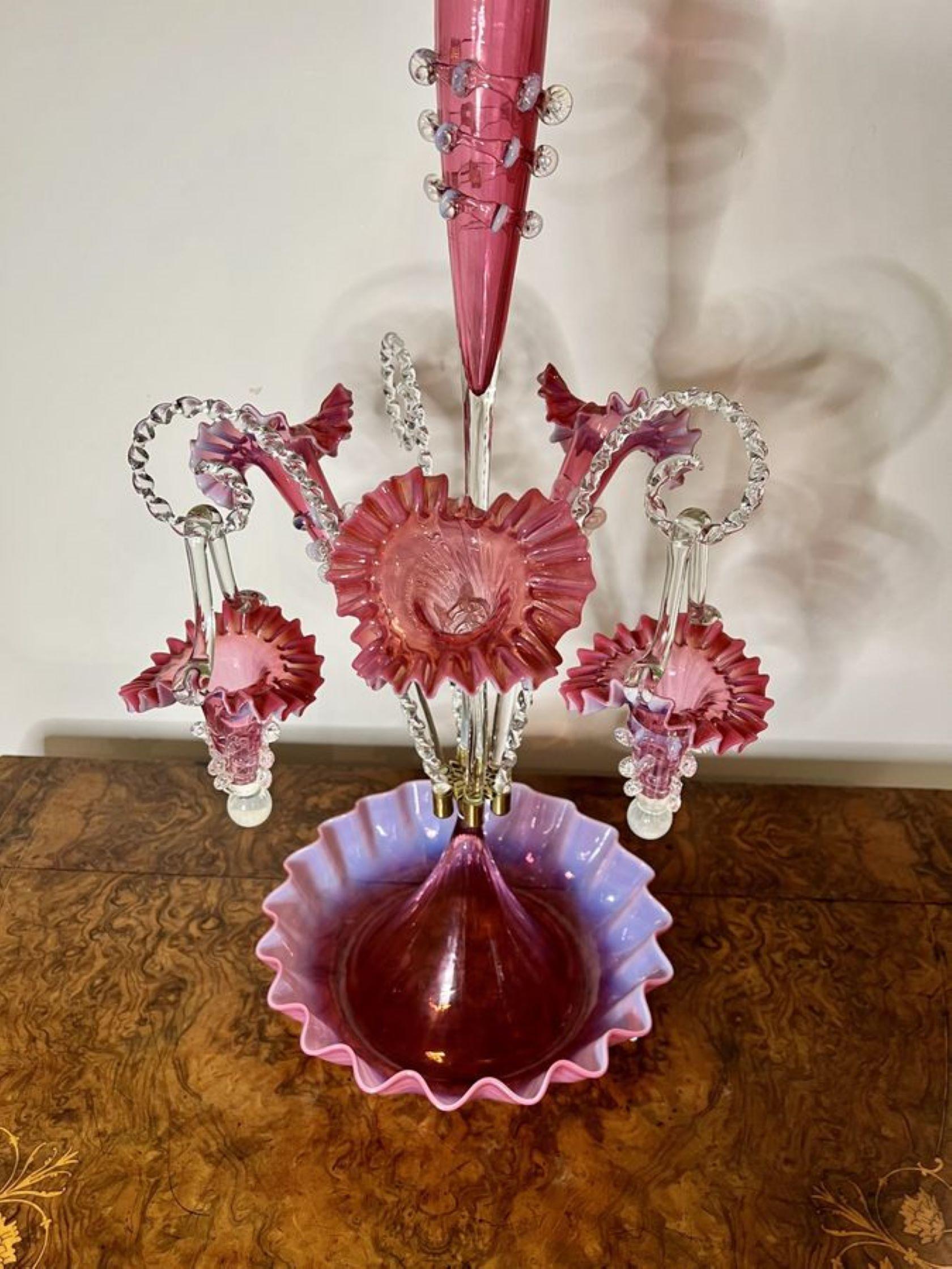 Outstanding quality large antique Victorian cranberry glass epergne having one tall trumpet to the centre, three smaller trumpet shaped flower holders and two hanging baskets on transparent shaped canes standing on a circular shaped wavy edge