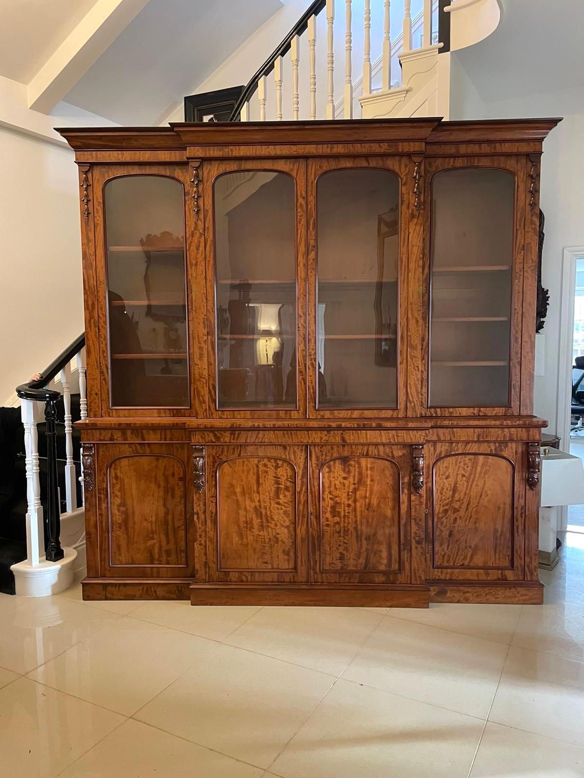 Outstanding quality large antique Victorian figured mahogany breakfront bookcase 
having an ogee shaped cornice above a figured mahogany breakfront shaped four door glazed top with quality carvings and eight adjustable shelves.  It boasts a