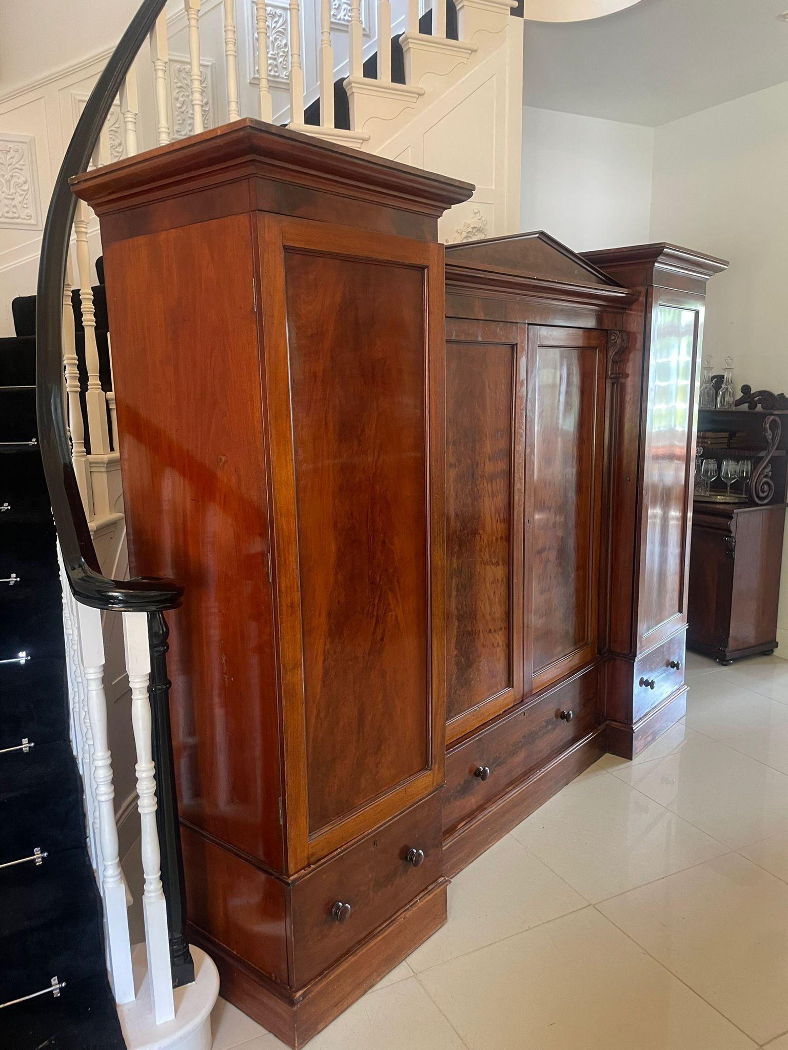 Outstanding quality large Victorian antique figured mahogany four door wardrobe having two moulded cornices and a figured mahogany pediment to the centre, two figured mahogany panelled doors below opening to reveal three storage shelves flanked by a