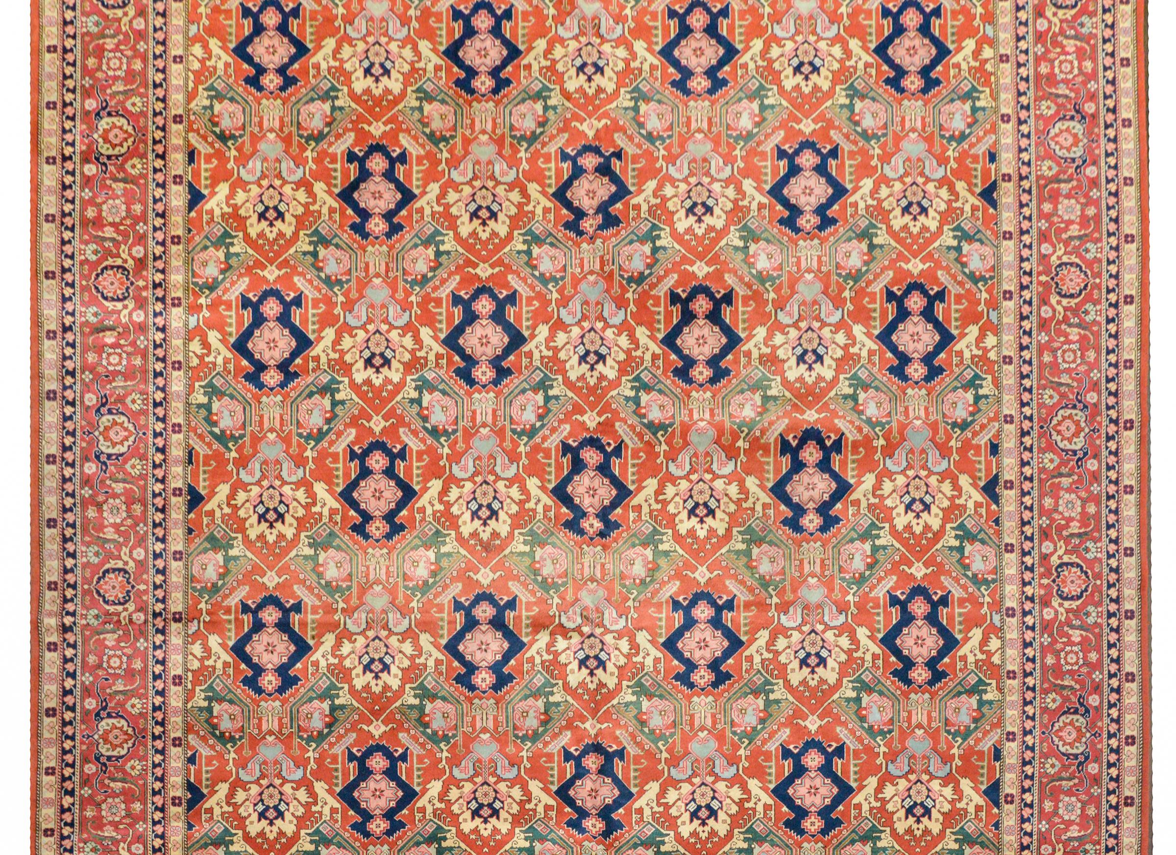 An outstanding vintage Romanian Serapi-style handwoven rug with a rare repeated stylized floral pattern woven in yellow, light and dark indigo, green, pink, and crimson, on a bold crimson background. The border is equally beautiful with a