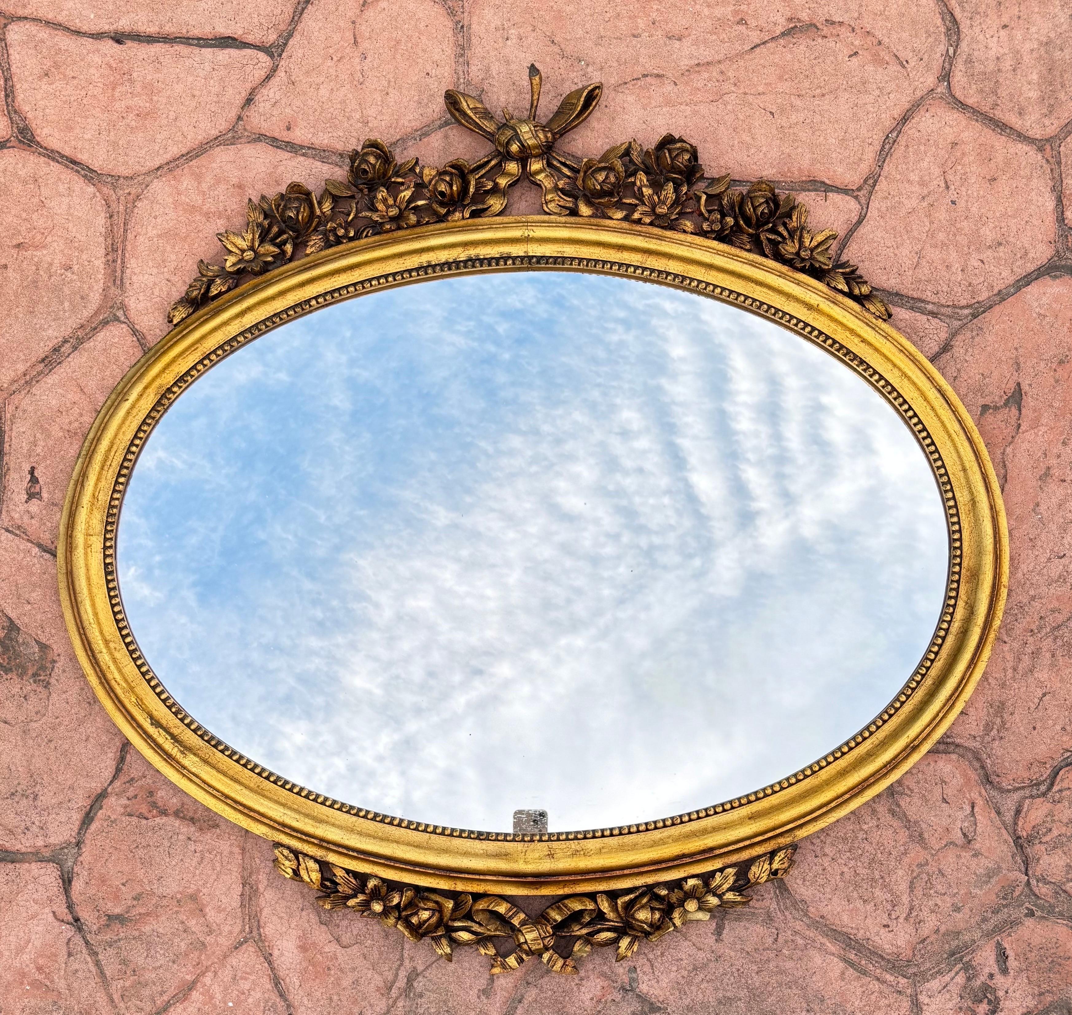 Français Miroir mural ovale des années 1940 avec cadre doré et décoration florale de style Louis XVI en vente