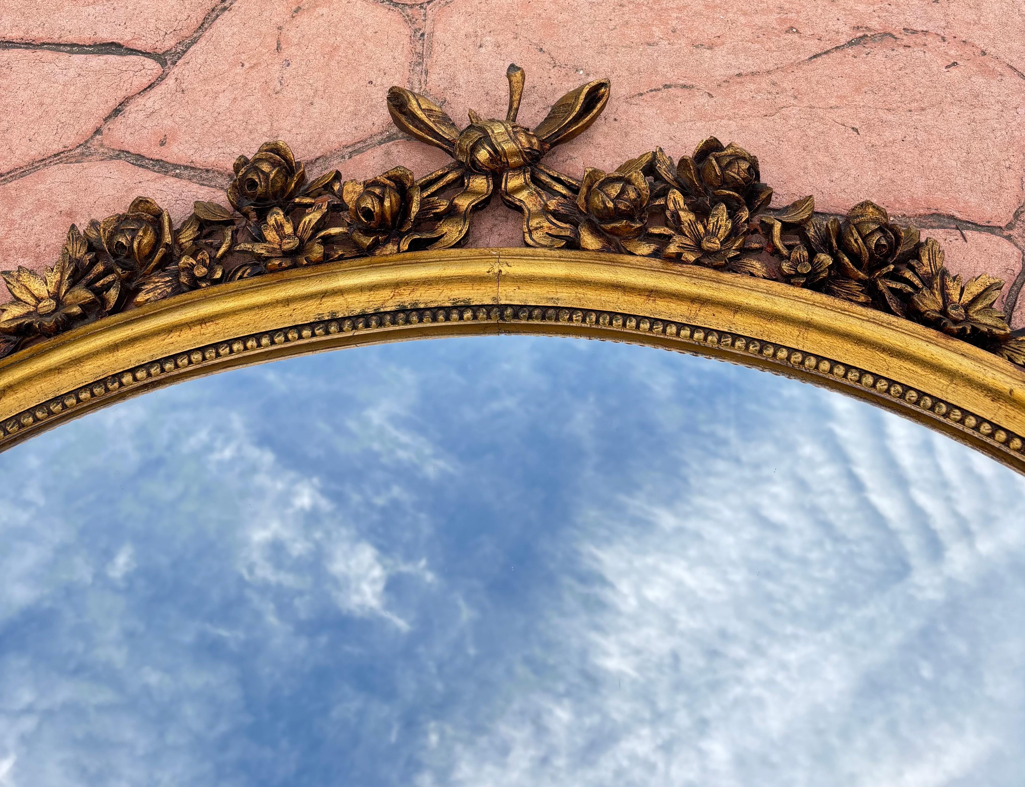 Sculpté à la main Miroir mural ovale des années 1940 avec cadre doré et décoration florale de style Louis XVI en vente