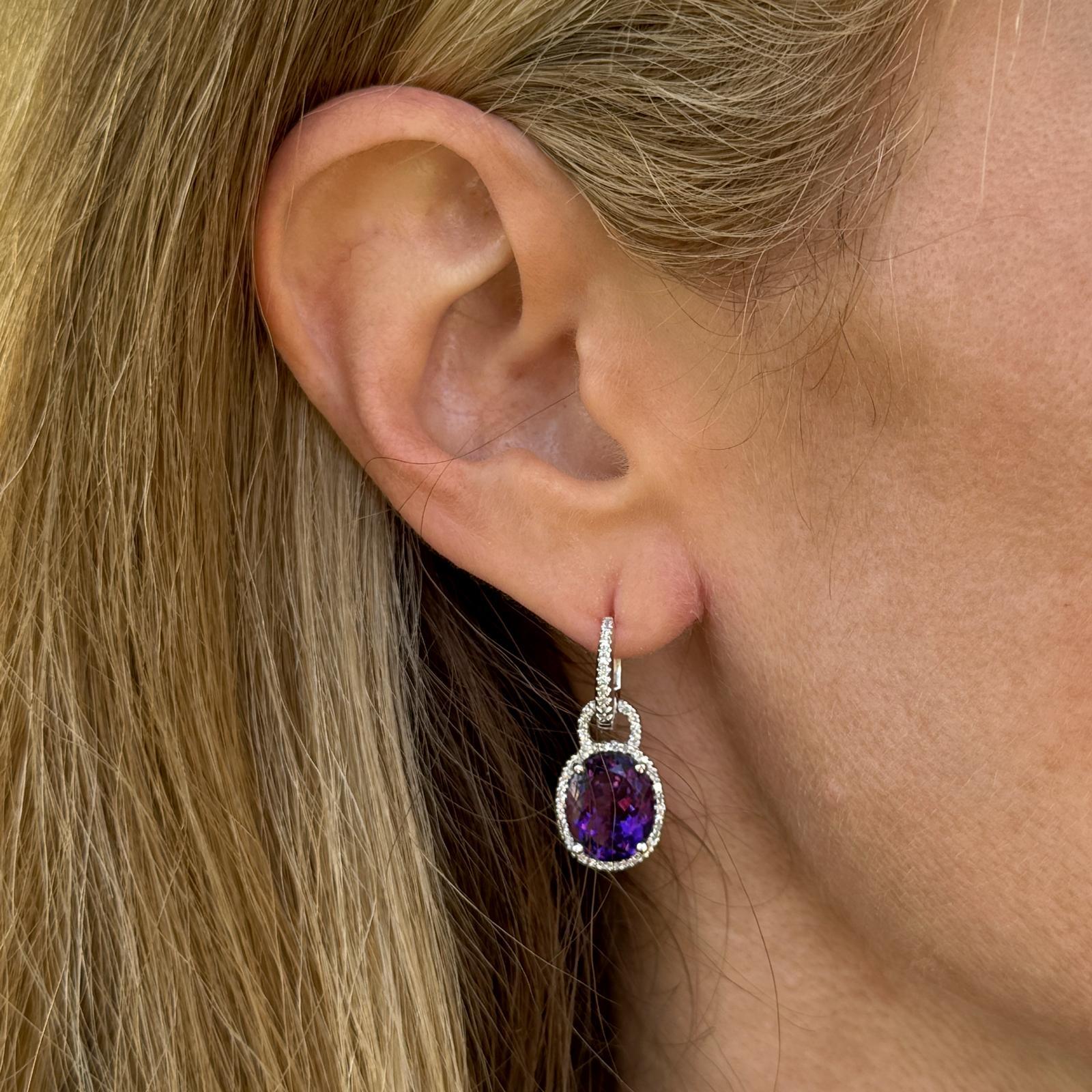 Diese eleganten und auffälligen Ohrringe aus 14-karätigem Weißgold sind mit zwei lebhaften Amethysten im Ovalschliff verziert, die einen satten violetten Farbton ausstrahlen. Die Edelsteine werden von ca. 88 funkelnden Diamanten im Einzelschliff von