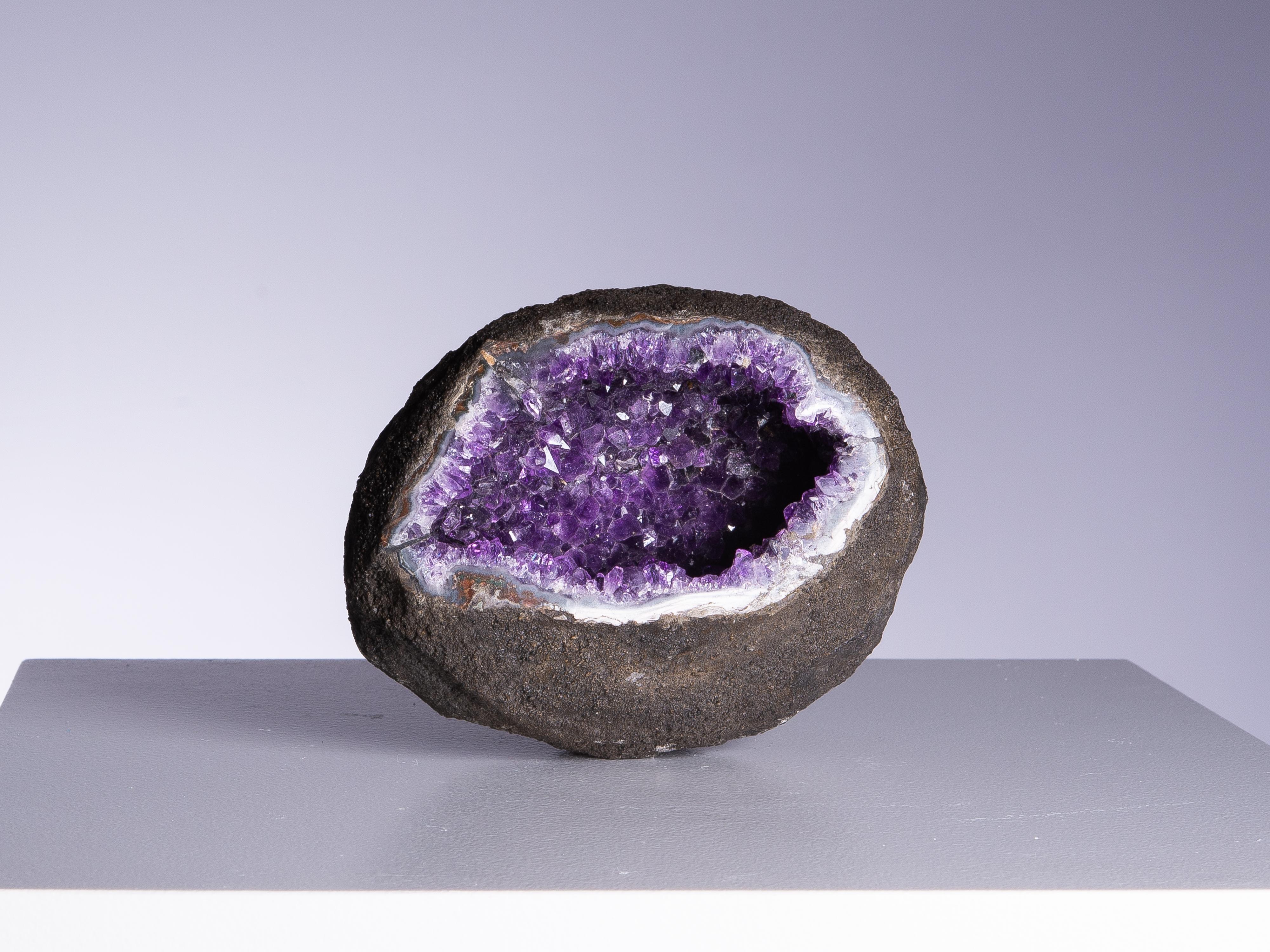 A gorgeous small oval amethyst geode with an eye-shaped aesthetic
opening revealing the high quality amethyst interior, creating a wonderful
contrast with the rough basalt exterior. The edges polished to reveal the
white quartz and blue agate