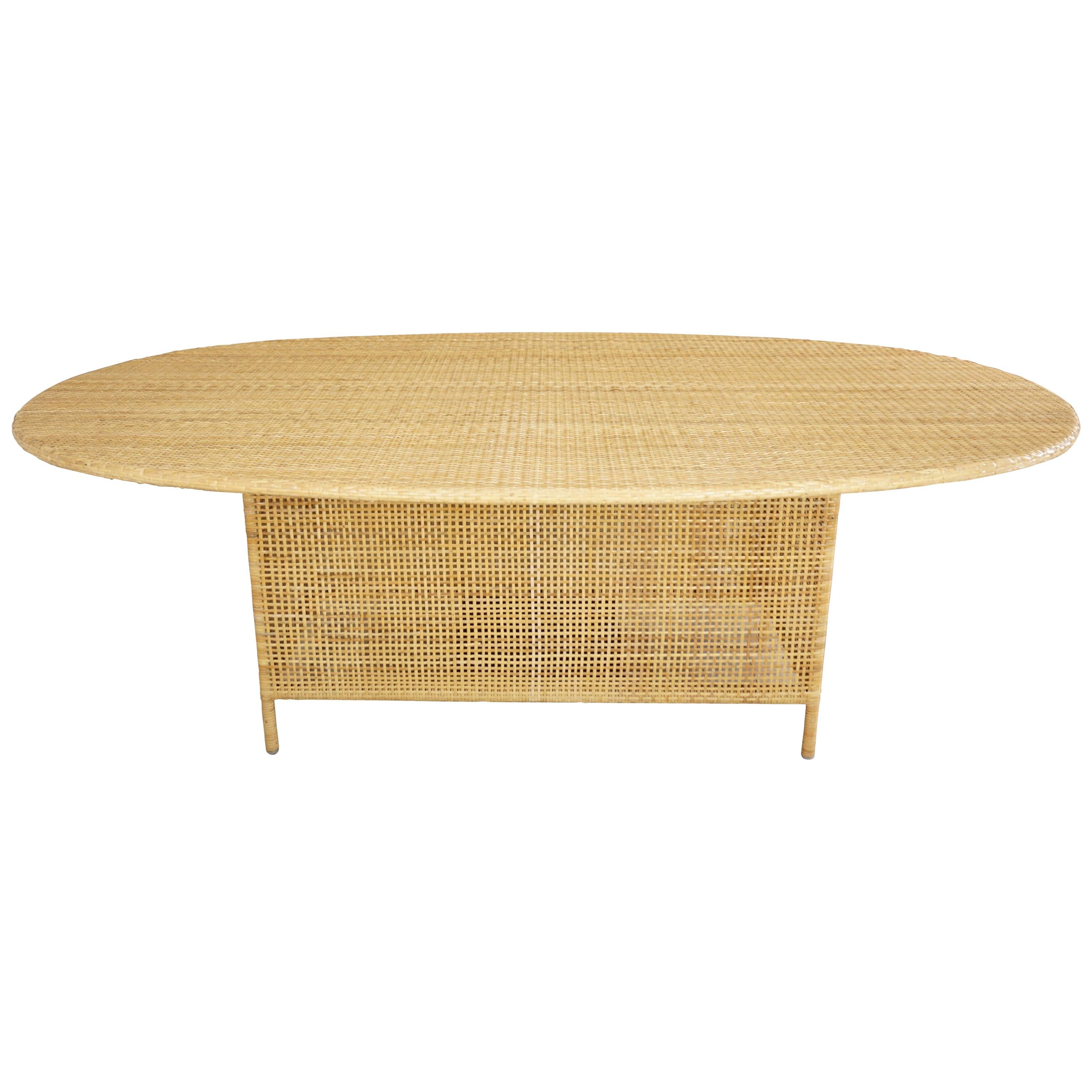 Oval and woven cane rattan French design dining table composed of a metal structure adorned with hand braided rattan. Elegance and transparency, aerial and Hollywood Regency style.