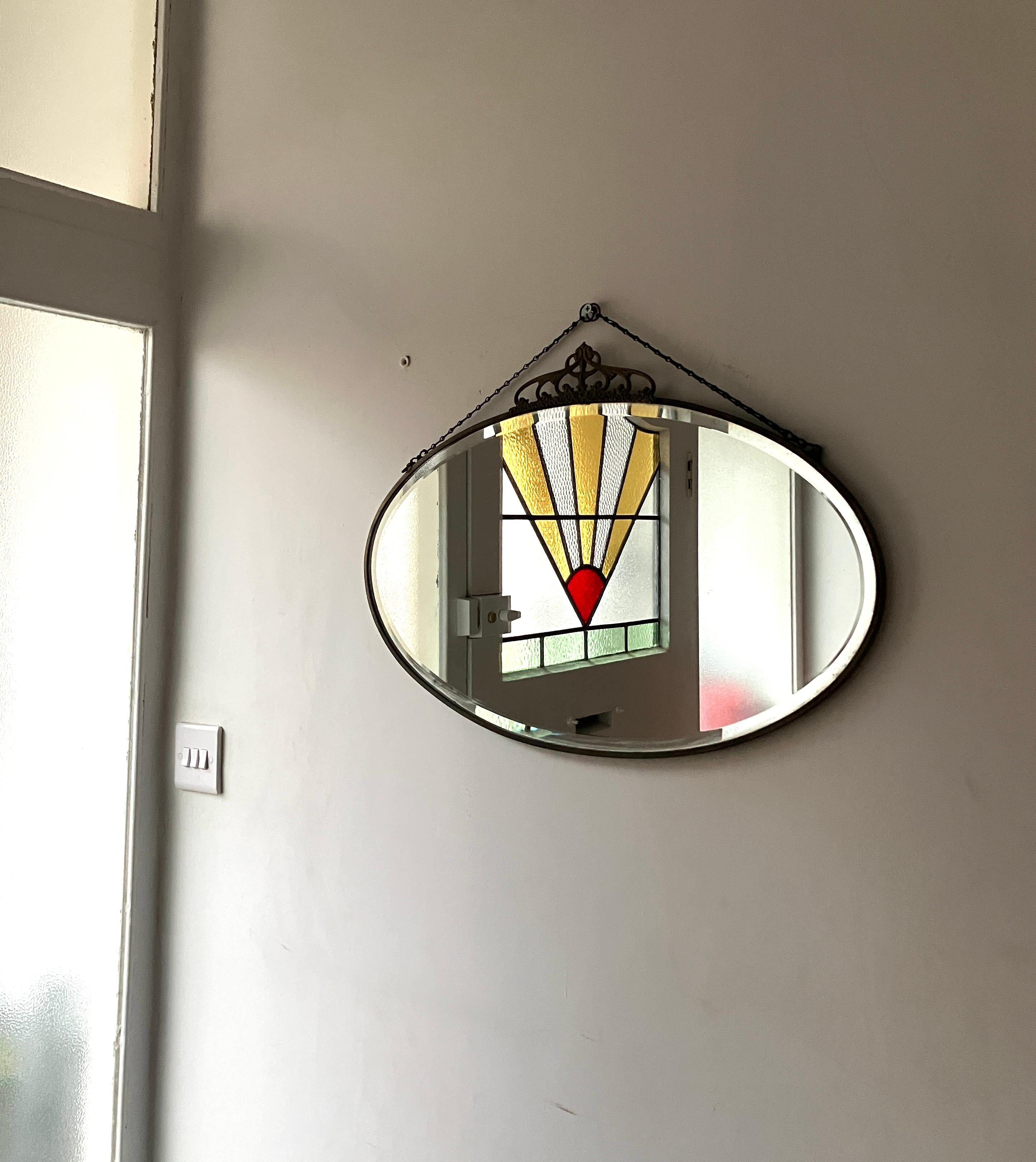 Beautiful antique oval wall hanging mirror from England. This oval mirror is brass framed with a decorative crown on top. There are maker marks at the back. Chain for hanging.

Size; 61cm wide, 35cm high plus 6cm for the crown. 

The mirror is in