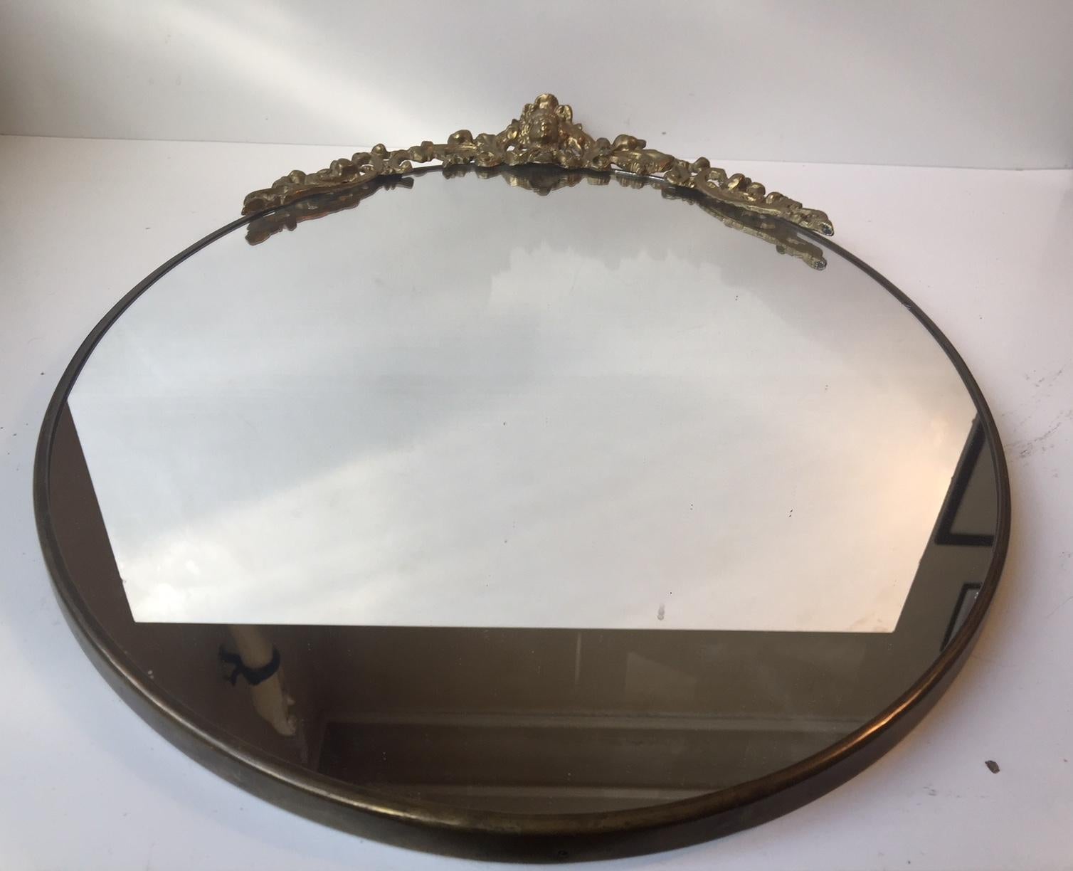 Oval wall mirror made of solid brass. Decorative head-piece with detailed ornamentation. This mirror was manufactured in Denmark in Louis XVI style. This mirror has been restored with a later wooden backplate within the last 40 years. The mirror