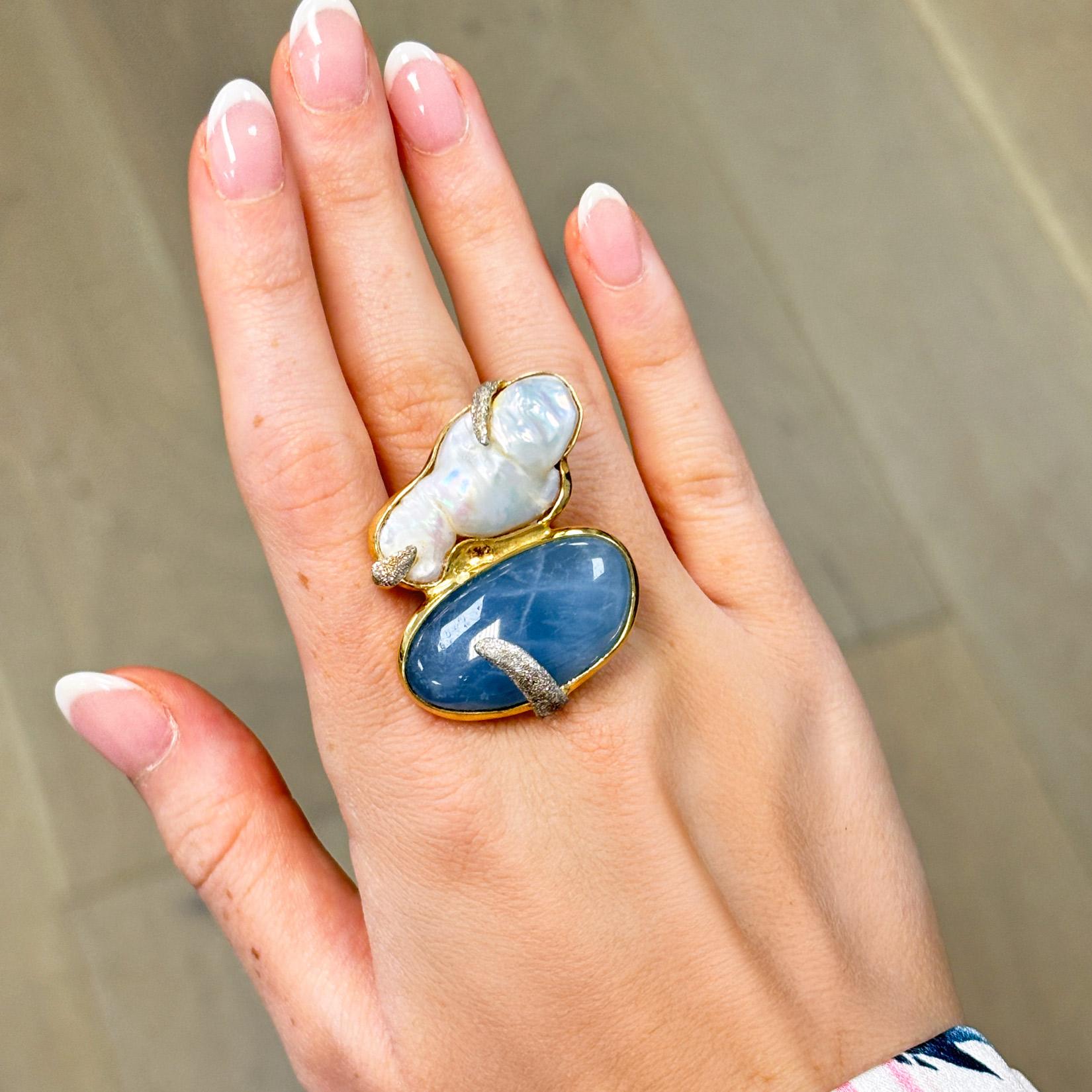 Eleganza con questo accattivante anello da cocktail, dove si incontrano tonalità serene e design senza tempo. Un'acquamarina ovale eterea è al centro della scena, graziosamente stratificata su madreperla per creare un bagliore morbido e iridescente.