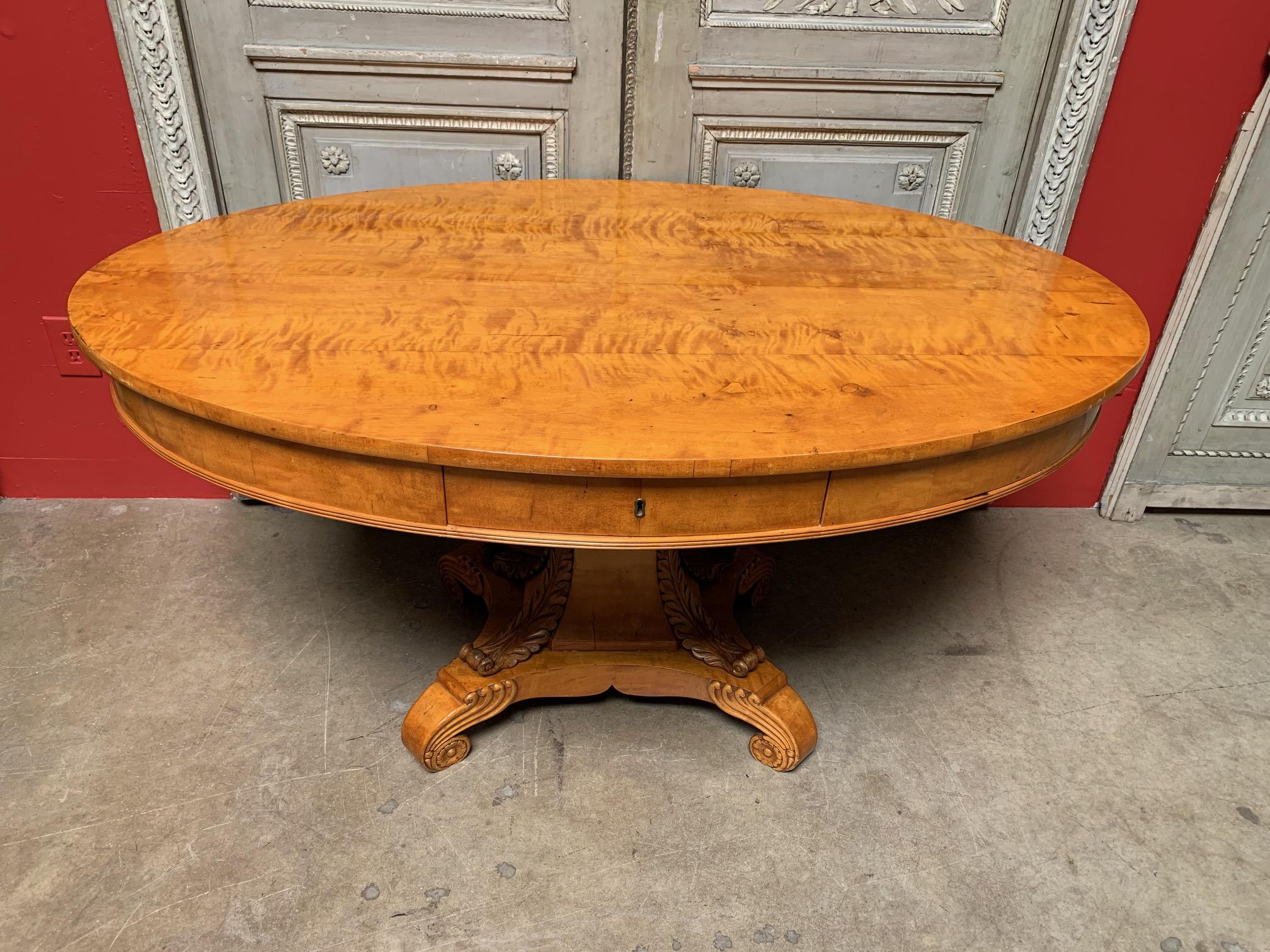 Oval Biedermeier maple library table with a pedestal base with acanthus leaf motif on four scrolled feet.