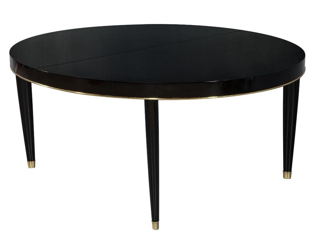 Beautiful oval gateau top dining table by Ralph Lauren. Accented with brass trim, elegant tapered legs and finished in polished black lacquer. Extends to 96” with one 24