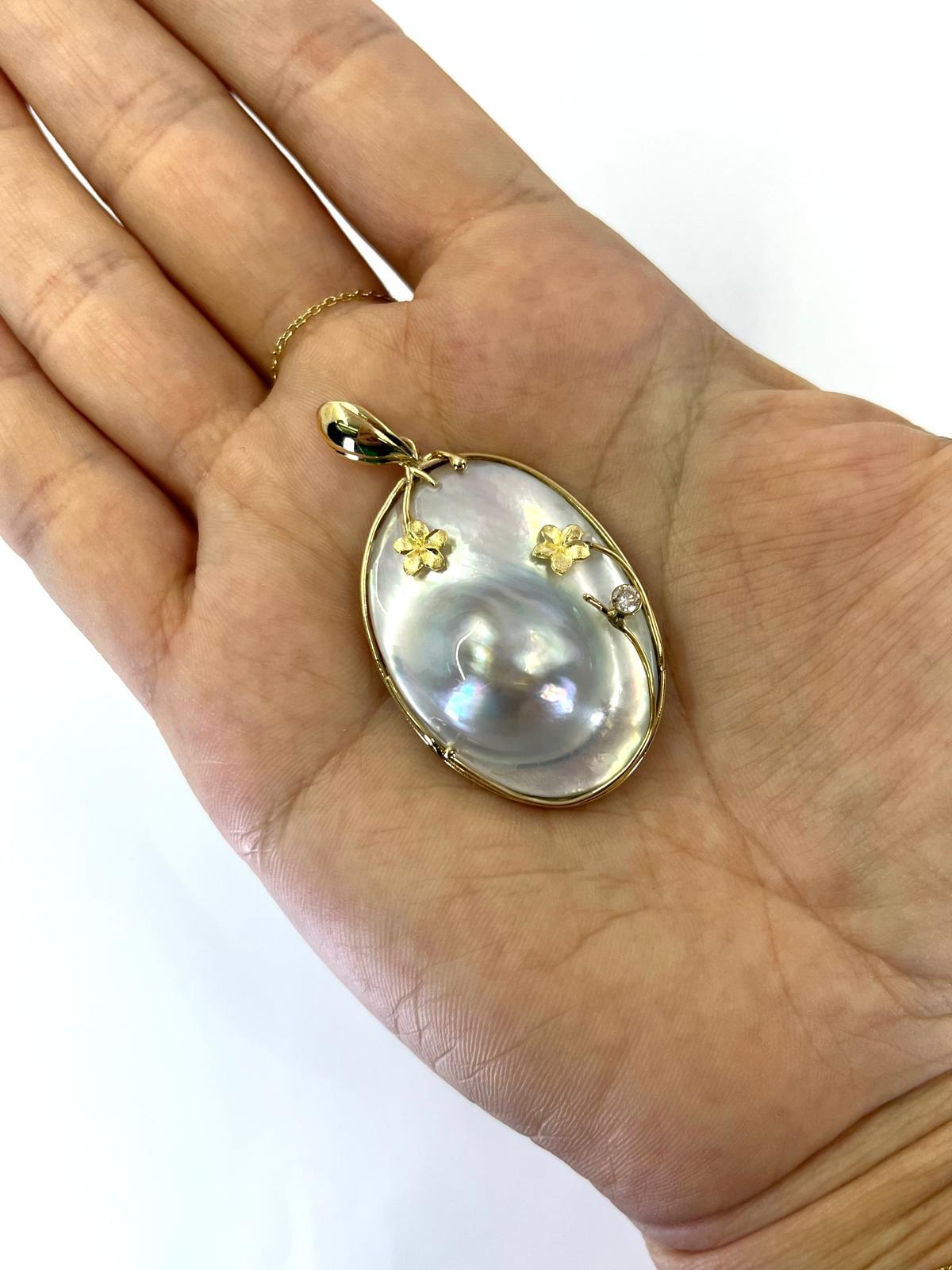 14 Karat Yellow Gold Oval Blister Pearl Pendant Featuring a Bezel Set Round Diamond of VS Clarity and H Color Weighing 0.10 Carats Accented by Flower Details. 2 Inches Long Including Bale. Finished Weight is 10.3 Grams.