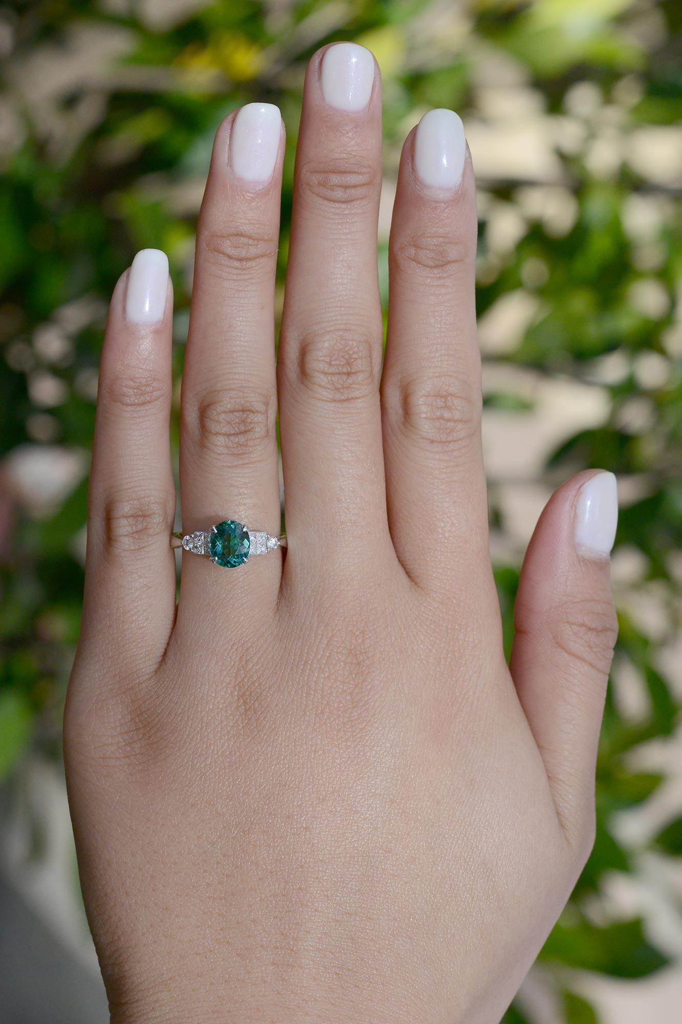 A rare and captivating blue-green (Indicolite) tourmaline gemstone engagement ring. The classic, staircase design 18kt. white gold setting featuring princess and round diamond accents creating a simple and clean look that sits low on your