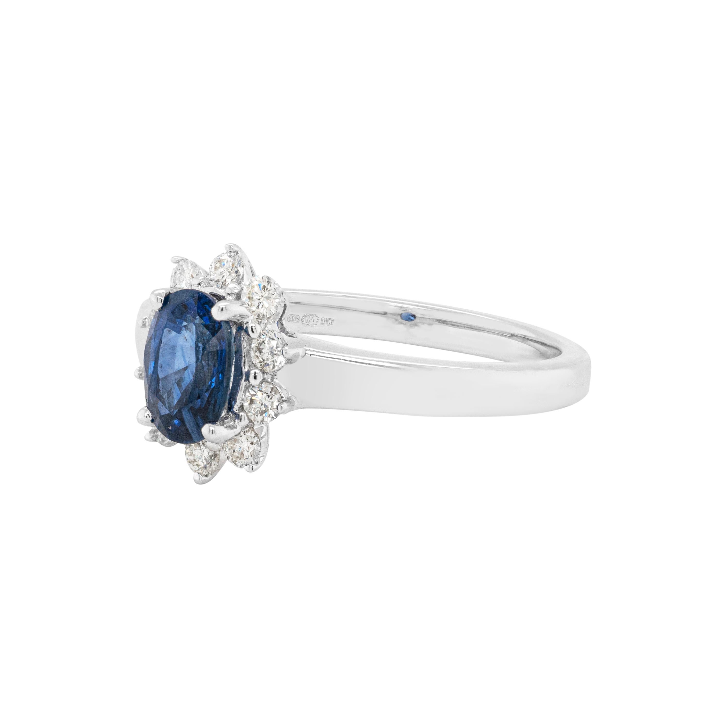 This lovely cluster engagement ring is beautifully centred with a royal blue oval sapphire weighing approximately 1.00 carats, mounted in a four claw, open back setting. The vivid stone is surrounded by 10 fine quality round brilliant cut diamonds