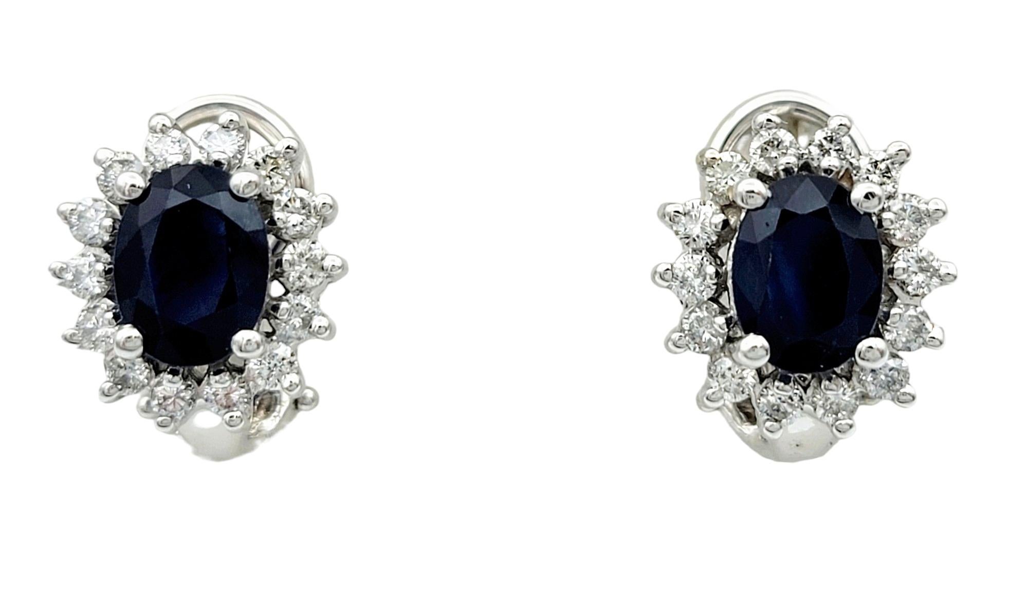 This gorgeous pair of oval blue sapphire stud earrings, adorned with a dazzling round diamond halo and set in elegant 14 karat white gold, epitomize sophistication and allure. Each earring features a captivating oval blue sapphire at its center,