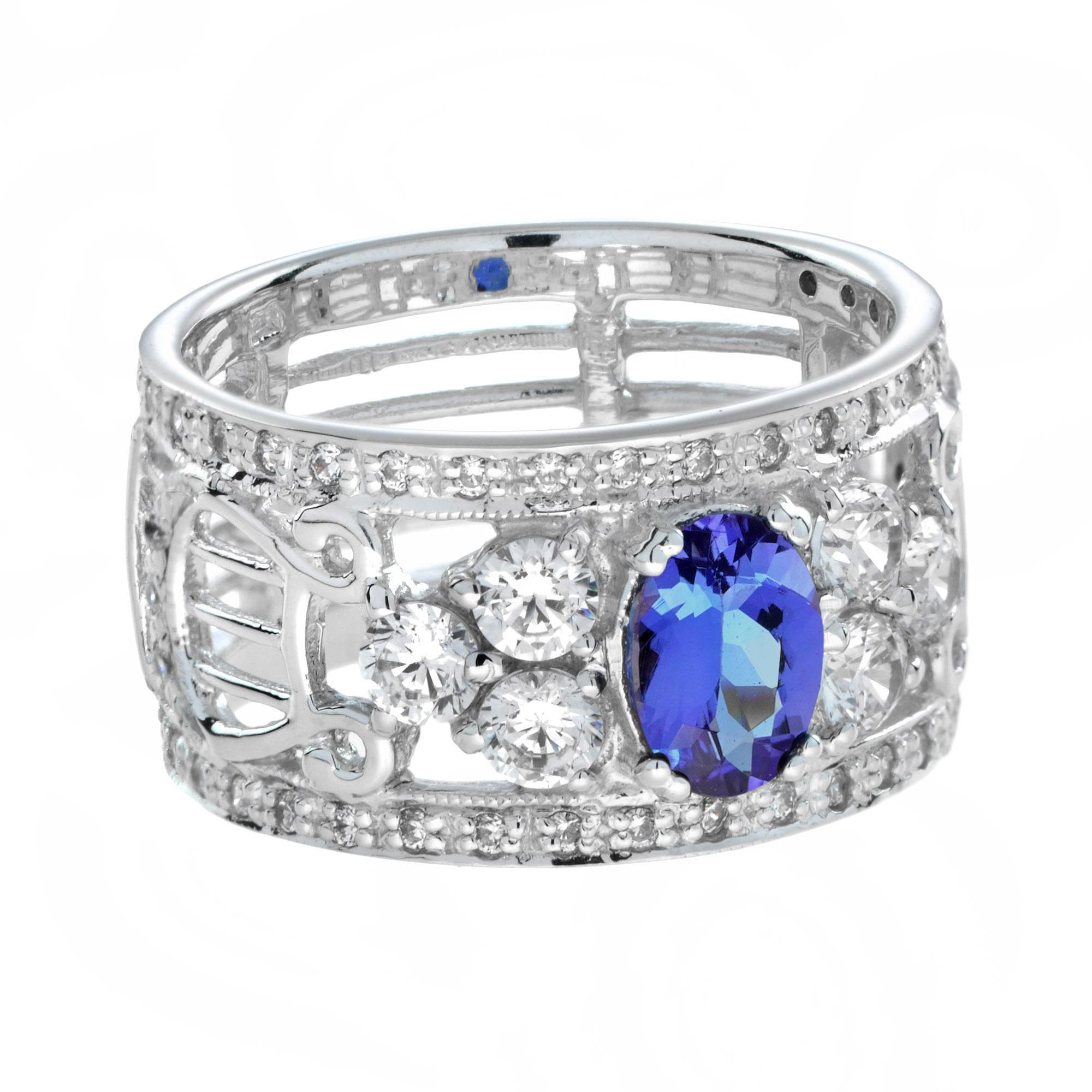 Deléitate con el epítome del lujo con este anillo de compromiso ancho estilo Art Decó de tanzanita y diamantes. Una fascinante tanzanita, con su cautivador tono azul-violeta intenso, ocupa el centro del escenario, rodeada de un halo de brillantes